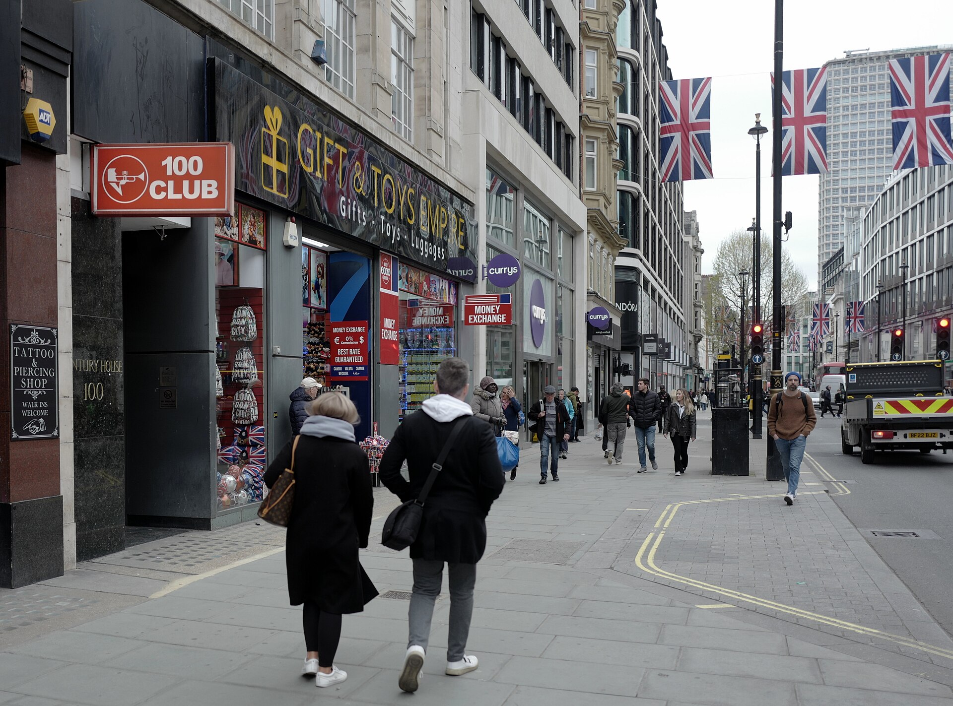 The red 100 Club sign hangs over a basement doorway on a busy Oxford Street pavement, Union Jack bunting strung overhead.