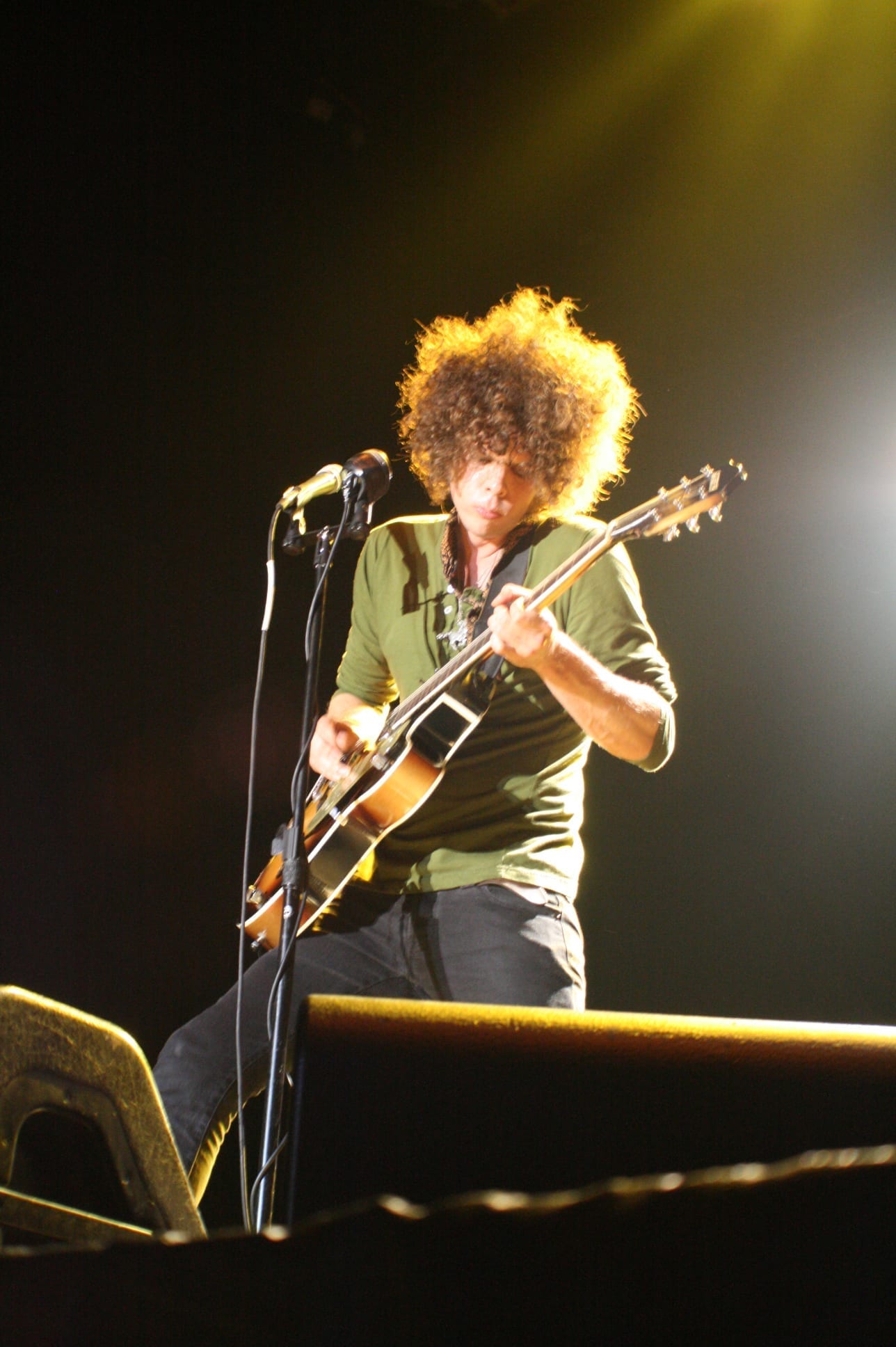 Andrew Stockdale plays a sunburst electric guitar and sings into a microphone on stage, his large curly hair backlit by yellow stage lighting.