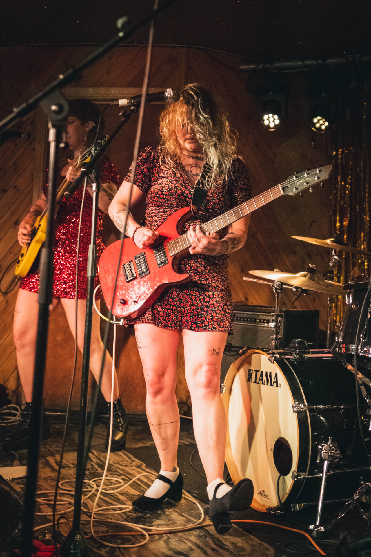 Two members of Bad Waitress play guitars side by side on a small club stage under warm lights.