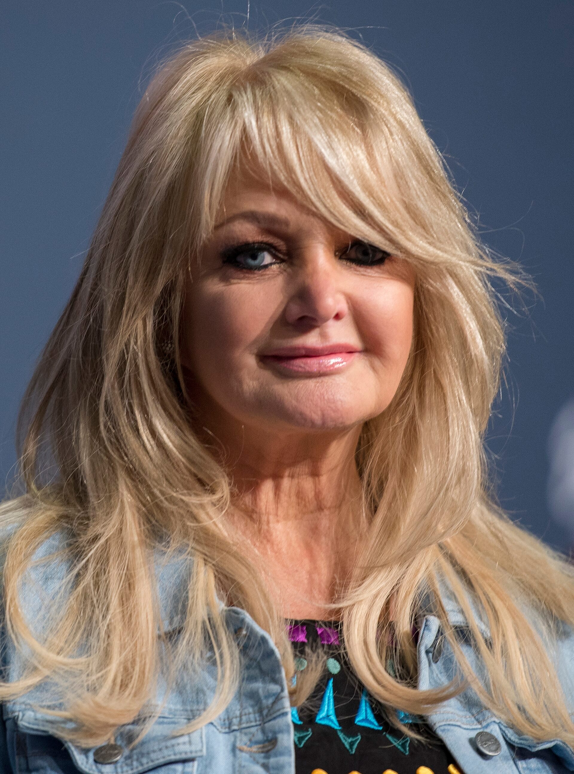 Bonnie Tyler, with long blonde hair and a denim jacket, looks at the camera at a press event.
