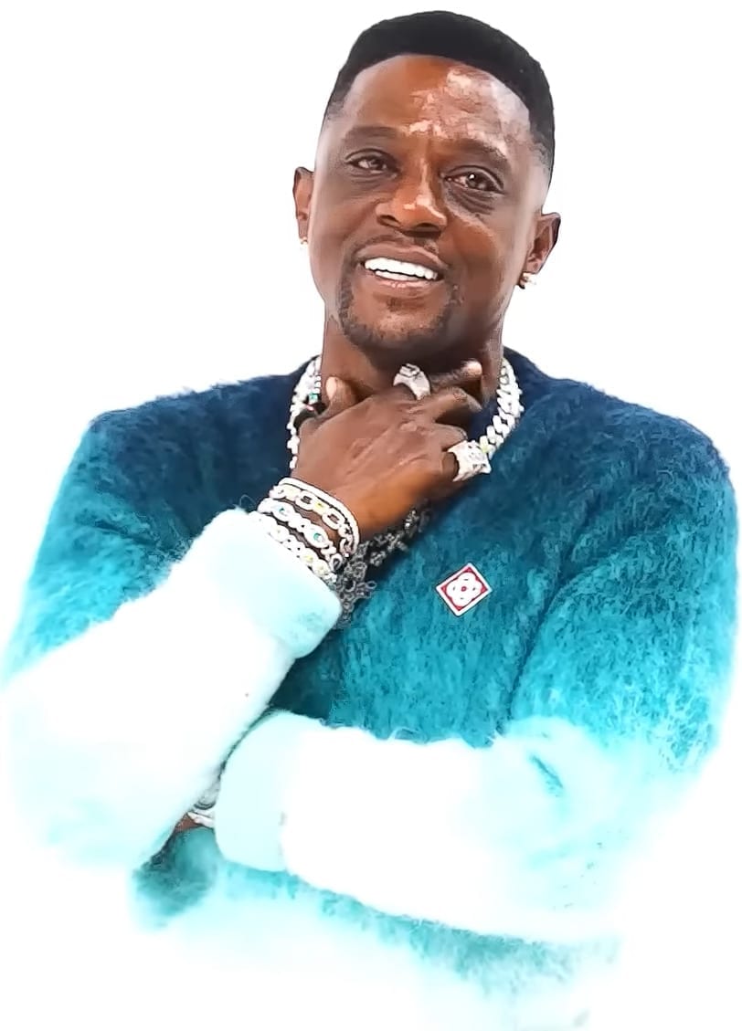 Boosie Badazz smiles with his hand near his chin, wearing a teal fuzzy sweater and layered gold chains and rings.