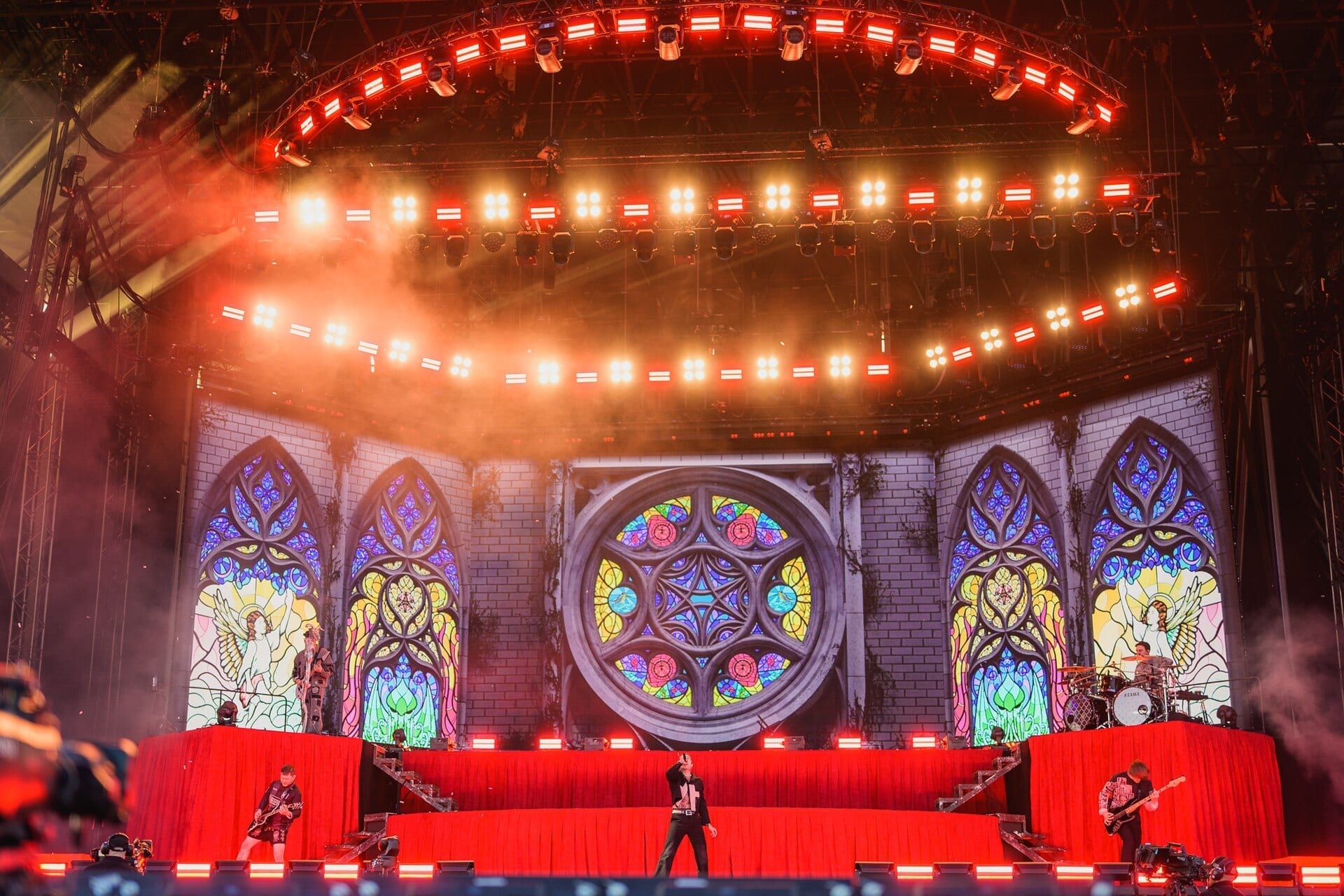 Bring Me The Horizon performs on a large festival stage framed by stained-glass-style screens, with the singer at center and band members on risers to each side.