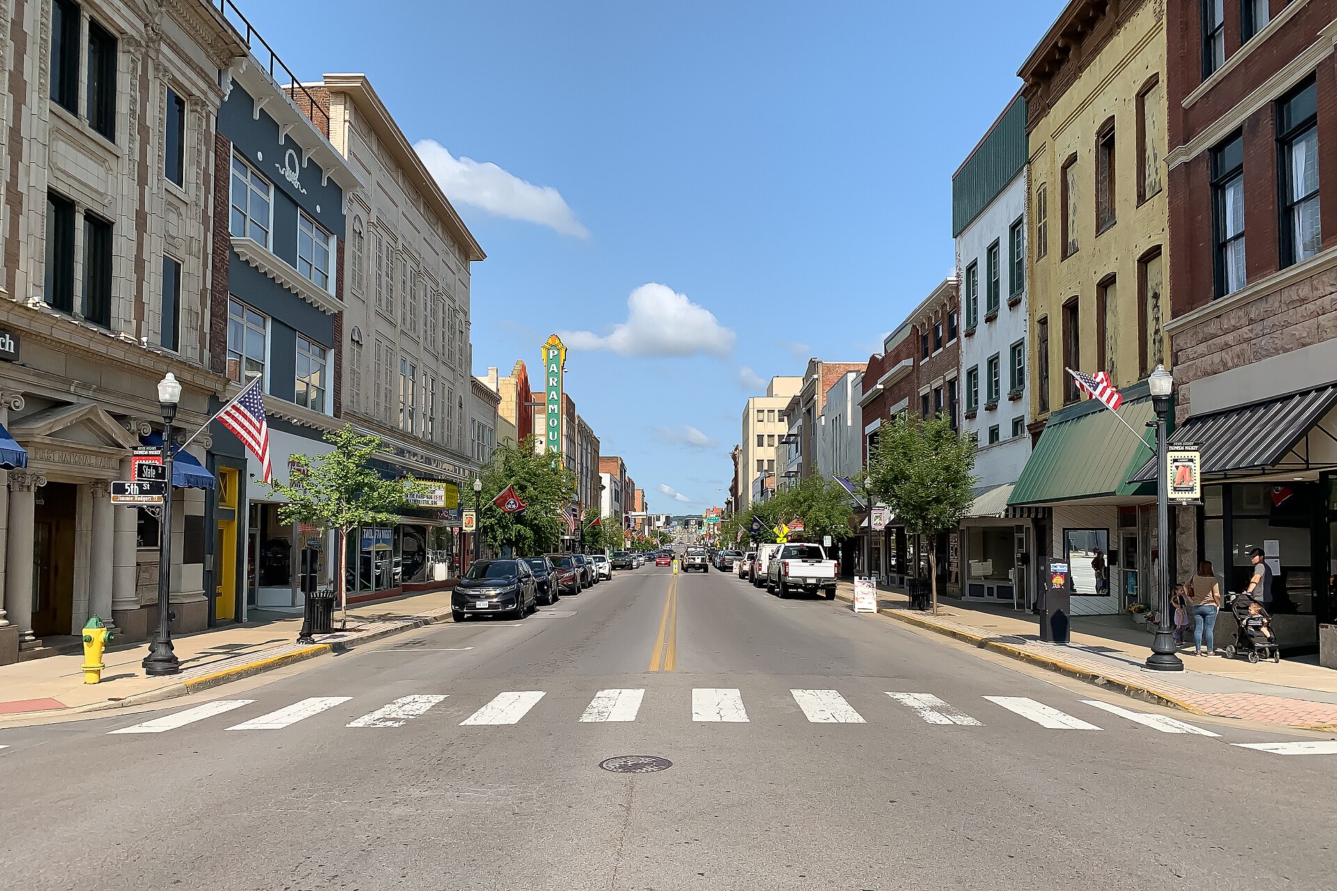 Looking down State Street in downtown Bristol on a clear day, brick and stone storefronts on both sides and the vertical Paramount theatre sign partway along the block