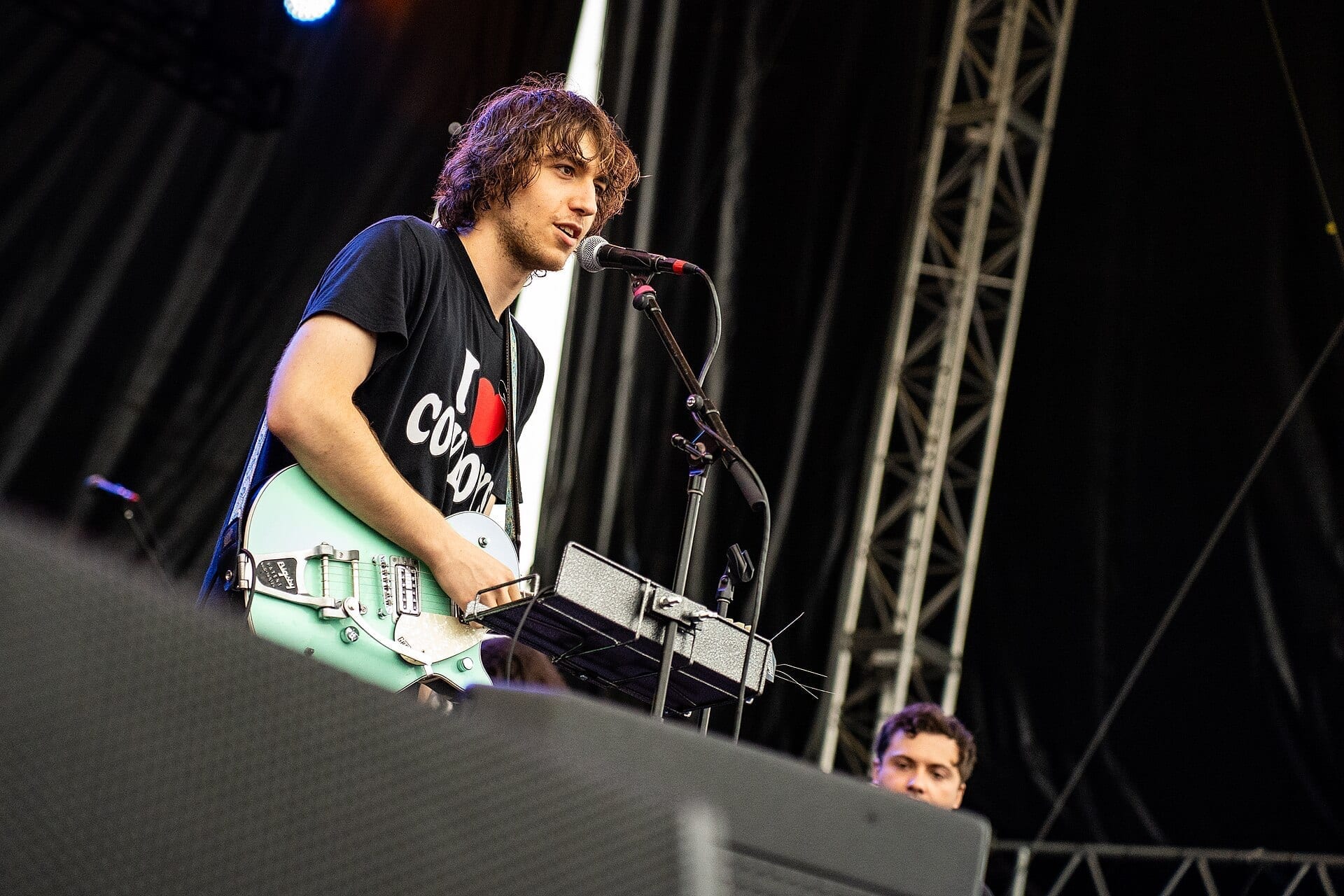 Cameron Winter sings into a microphone while playing a mint-green electric guitar on an outdoor festival stage.