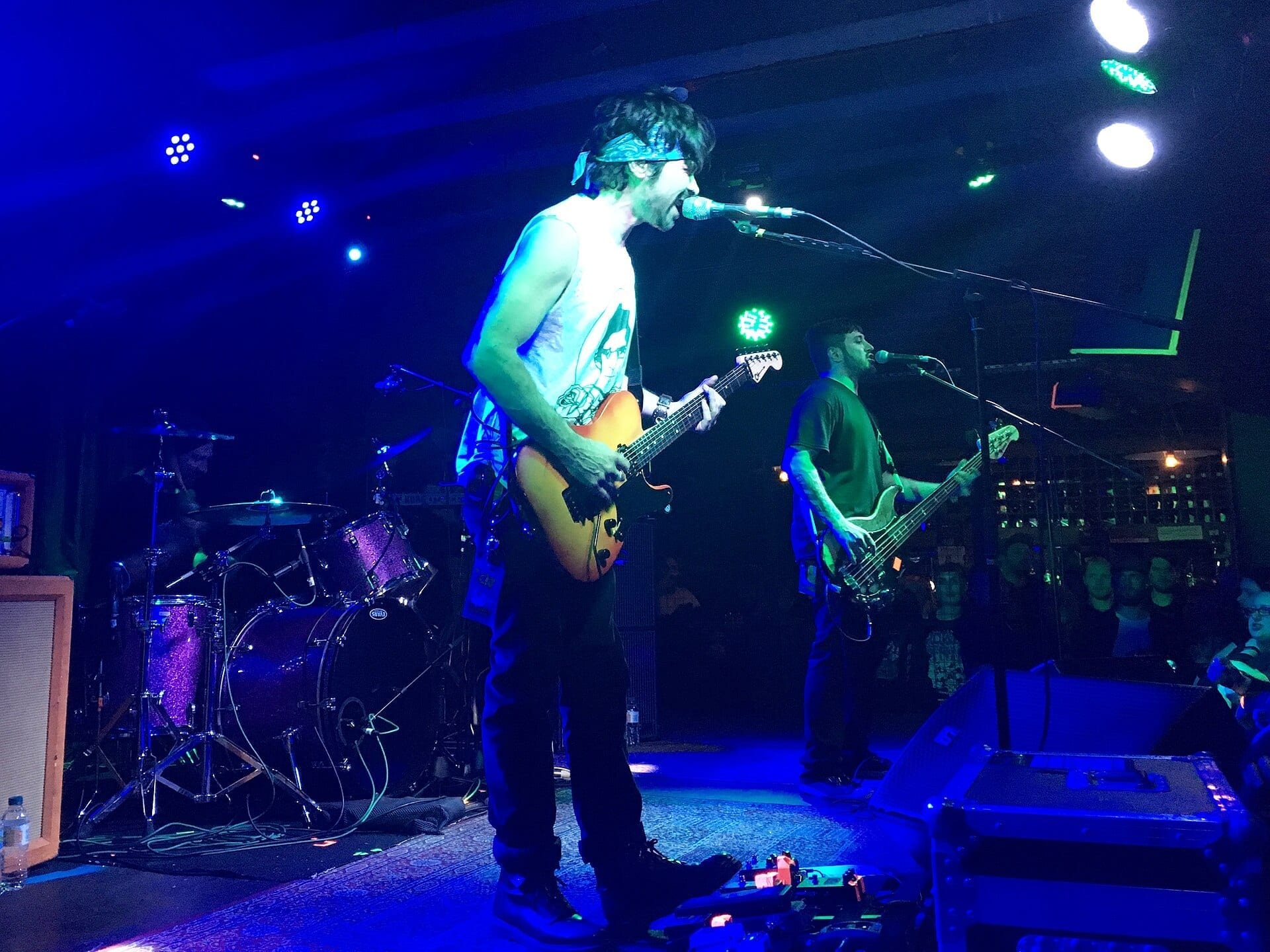 CKY performs on stage under blue and green lights, with the guitarist singing into a microphone and the bassist playing behind him.