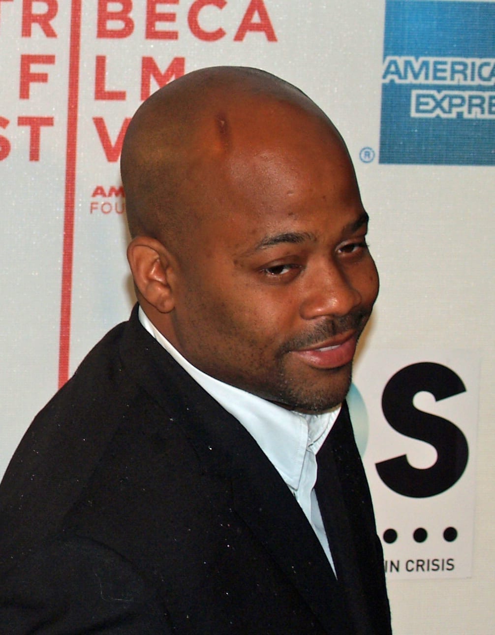 Damon Dash, wearing a black suit and white shirt, glances over his shoulder at a Tribeca Film Festival step-and-repeat backdrop.