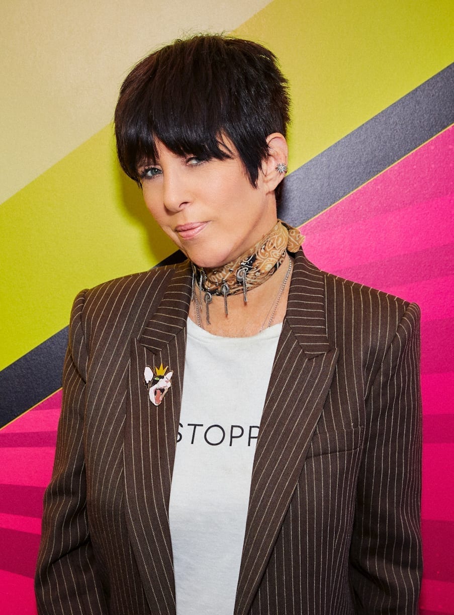 Diane Warren, in a pinstriped blazer and patterned scarf, poses in front of a colorful geometric backdrop.