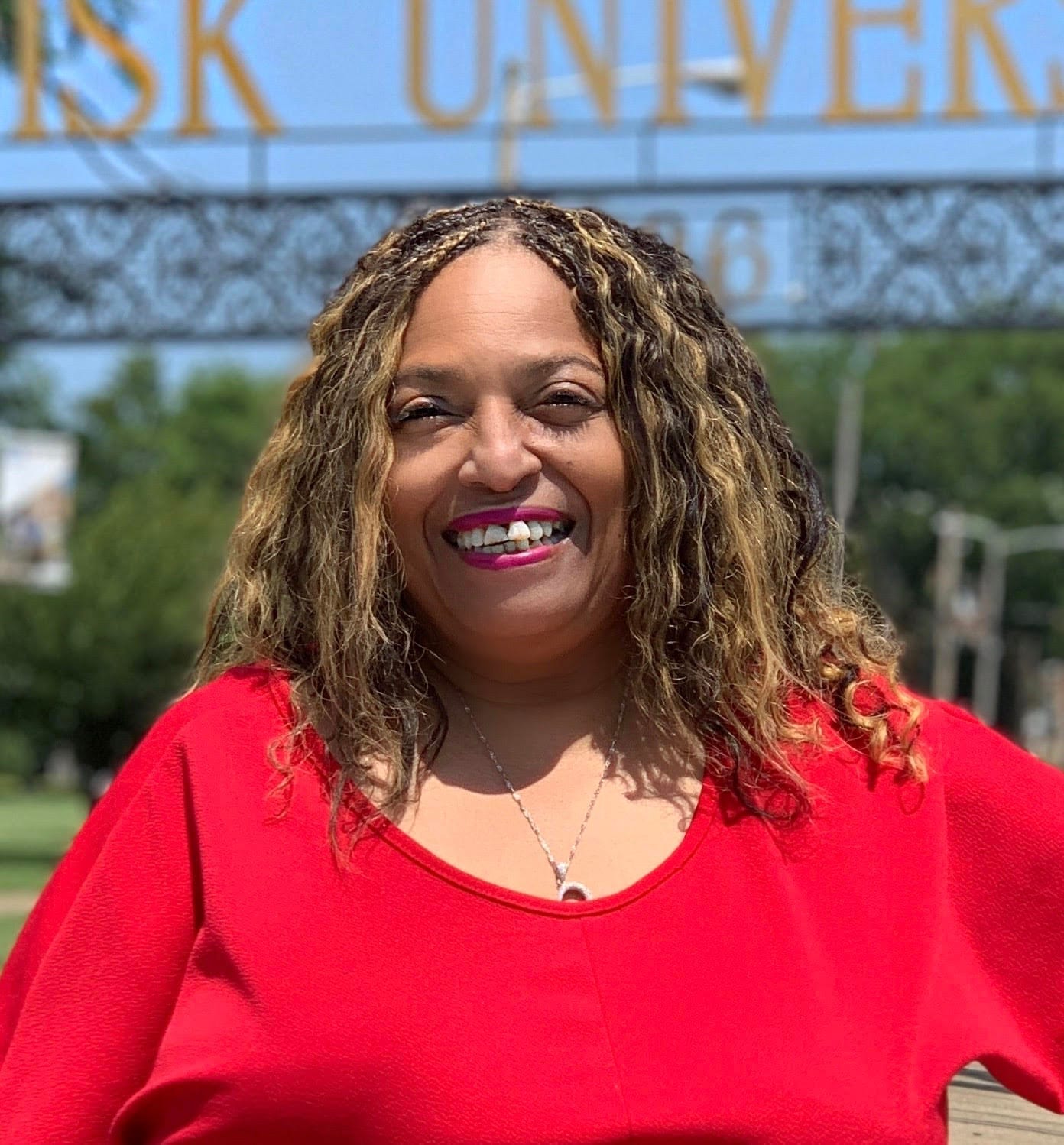 Flo Anthony smiles in a red top, standing outdoors in front of a Fisk University sign.