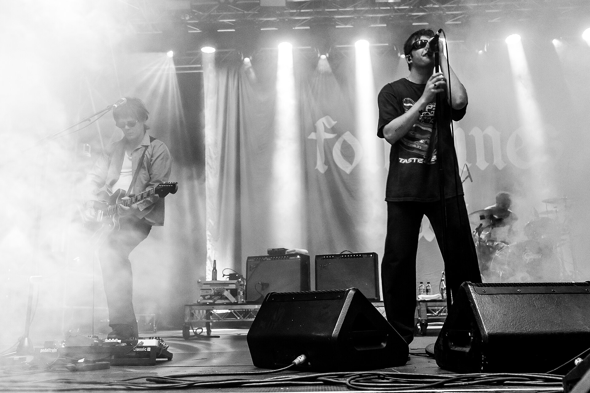 Fontaines D.C. onstage in black and white, the singer bent over a microphone stand at the front with a guitarist beside him.