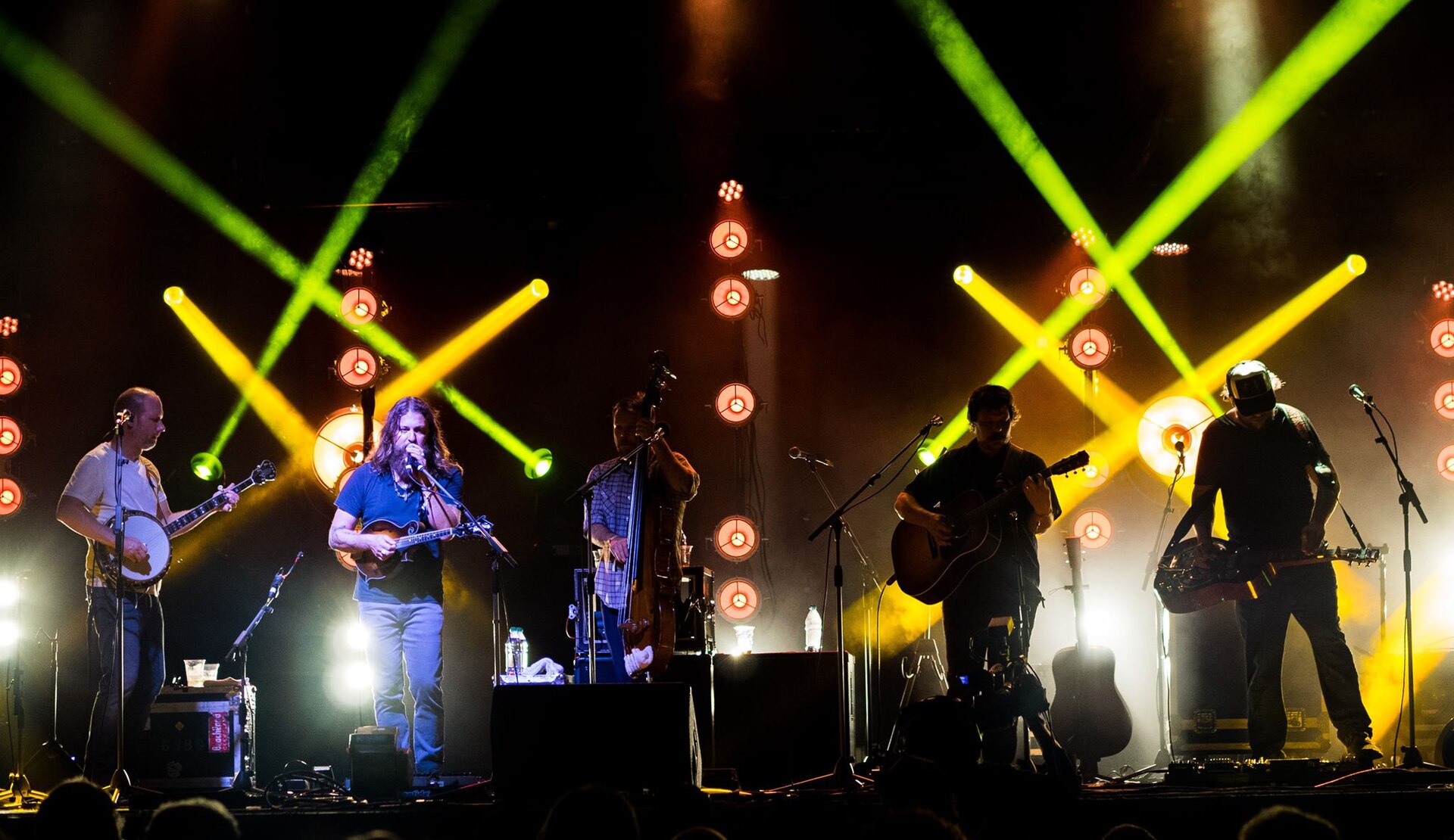 Greensky Bluegrass play across a festival stage with banjo, mandolin, upright bass, acoustic guitar and dobro, green and yellow beams crossing overhead.