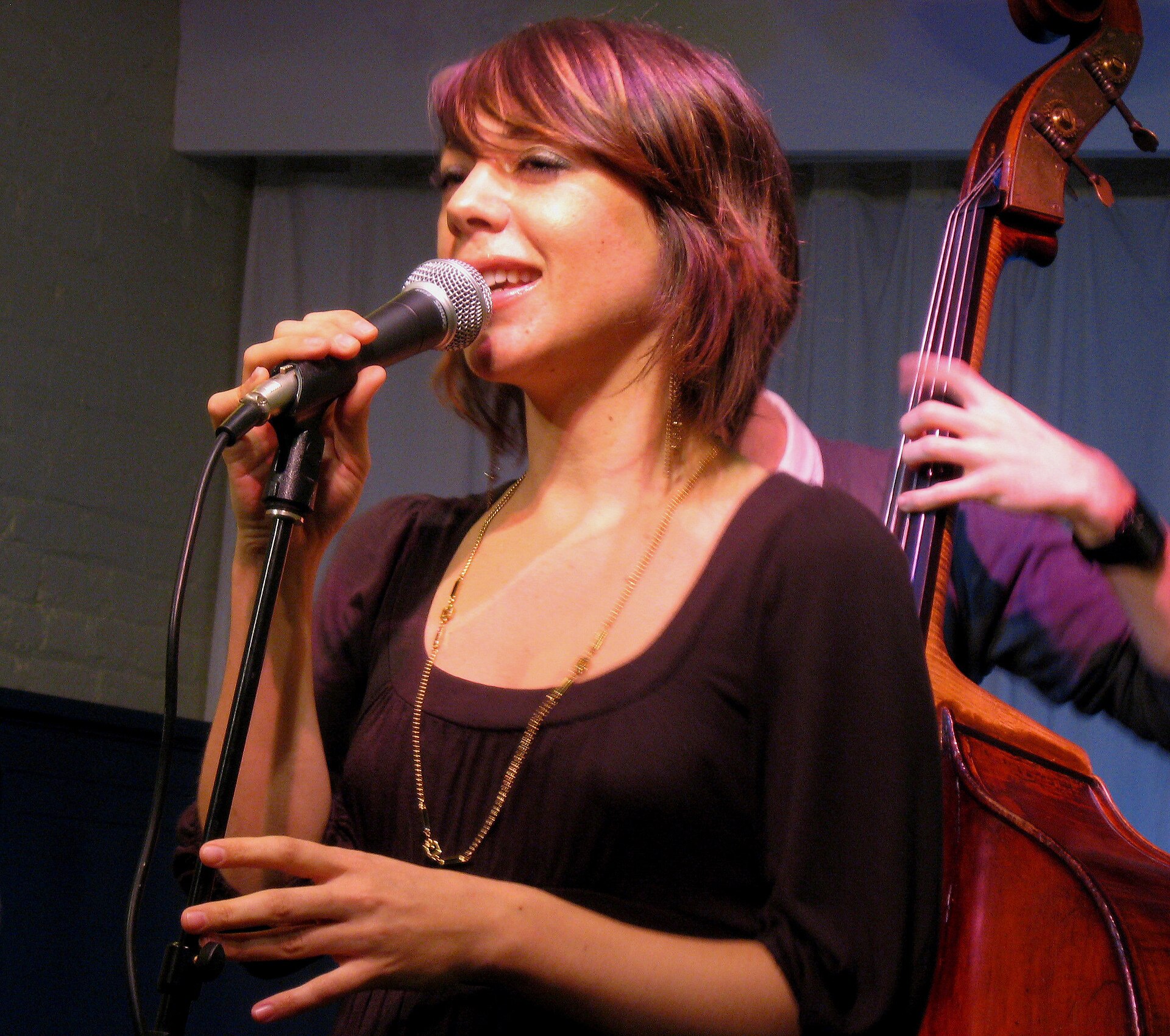 Gretchen Parlato sings into a microphone on a stand with a double bassist playing just behind her.