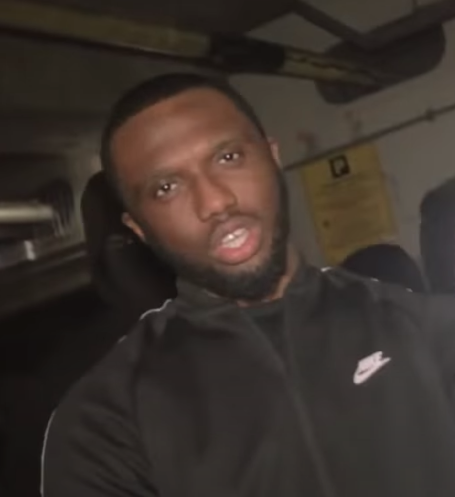 Headie One talks to camera in a black zip-up tracksuit top in a still from a video interview.