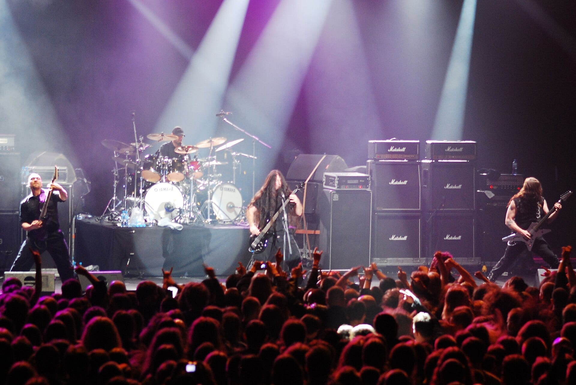 Immolation performs on a large festival stage with a wall of Marshall amps behind them, playing to a crowd throwing up horns under purple lights.