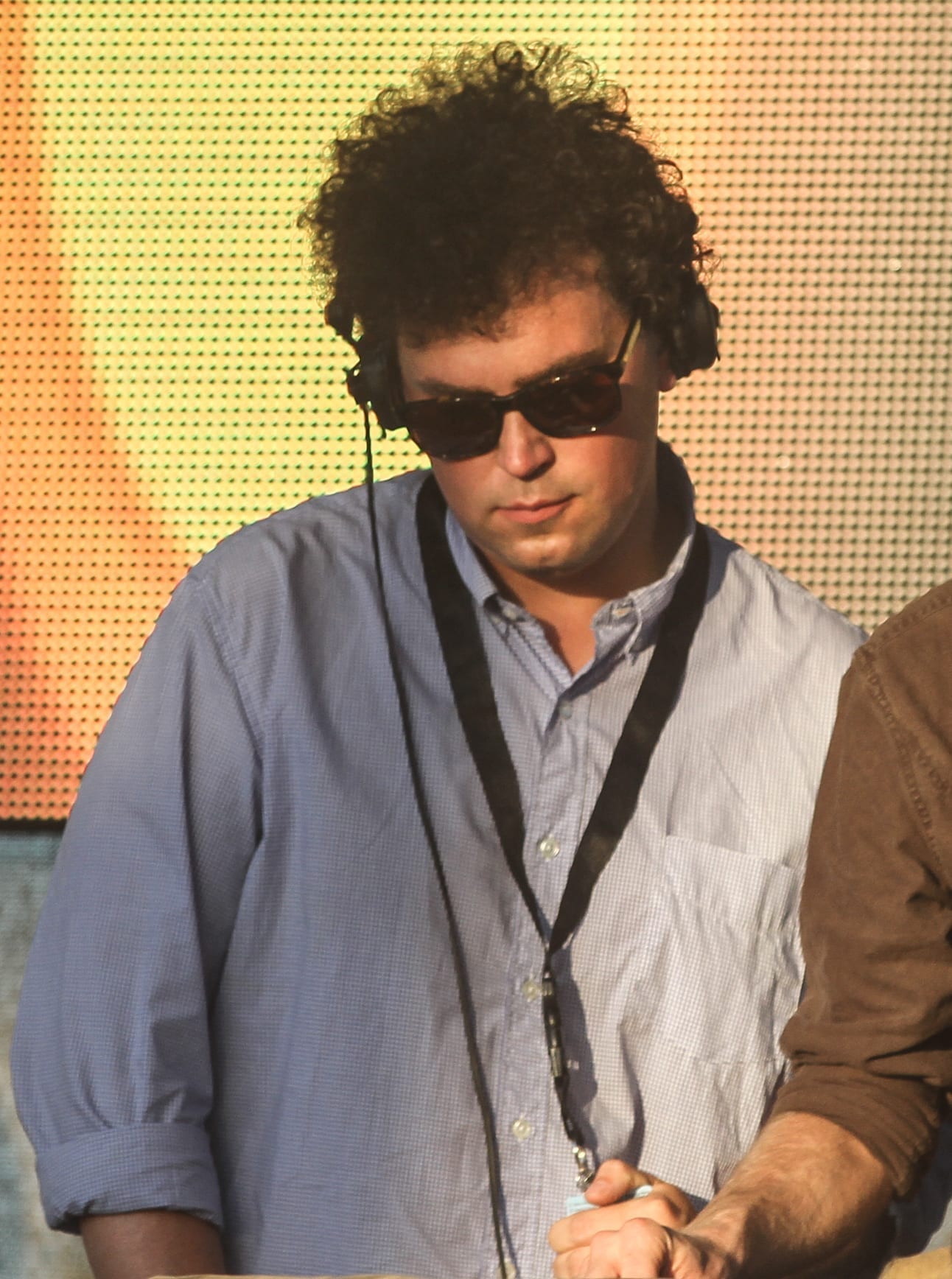 James Ellis Ford, wearing sunglasses and headphones around his neck, standing at a mixing setup outdoors.