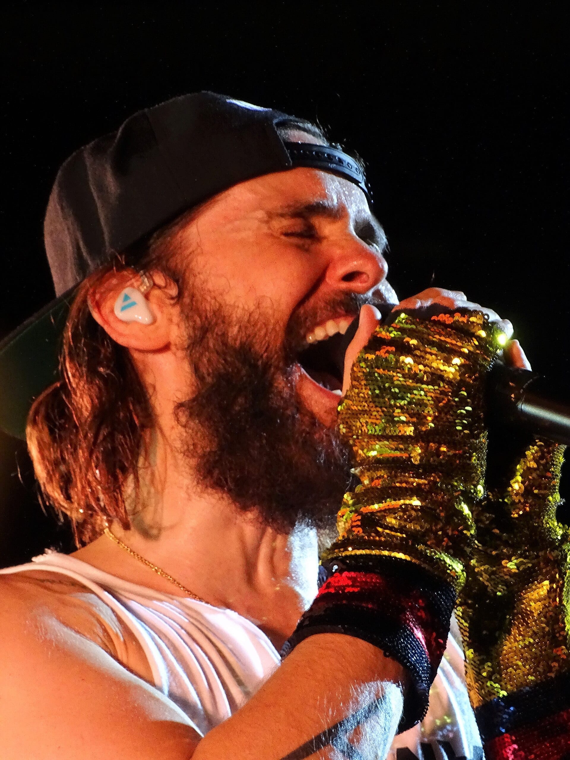 Jared Leto, bearded and wearing a backward cap, screams into a gold sequined microphone on stage.
