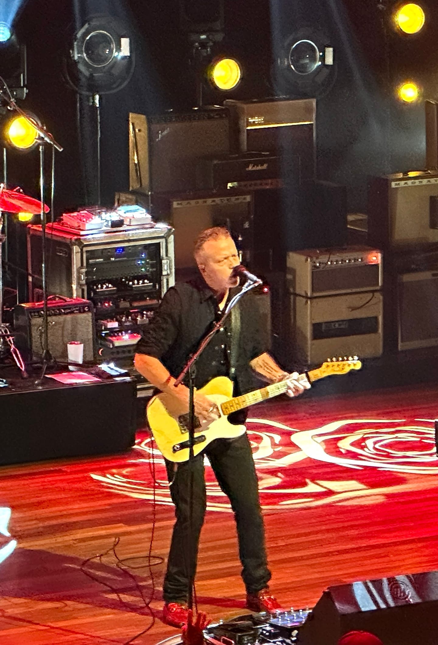 Jason Isbell sings at a microphone while playing a cream-colored electric guitar on the Ryman Auditorium stage.