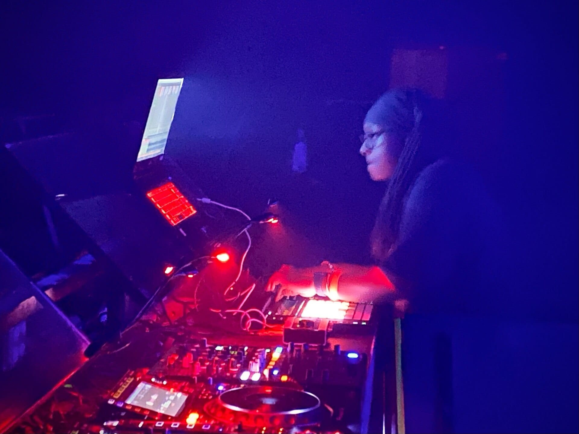 Jlin works over a laptop and a bank of controllers in a dark club, her face lit by the screen while red light picks out the pads in front of her.
