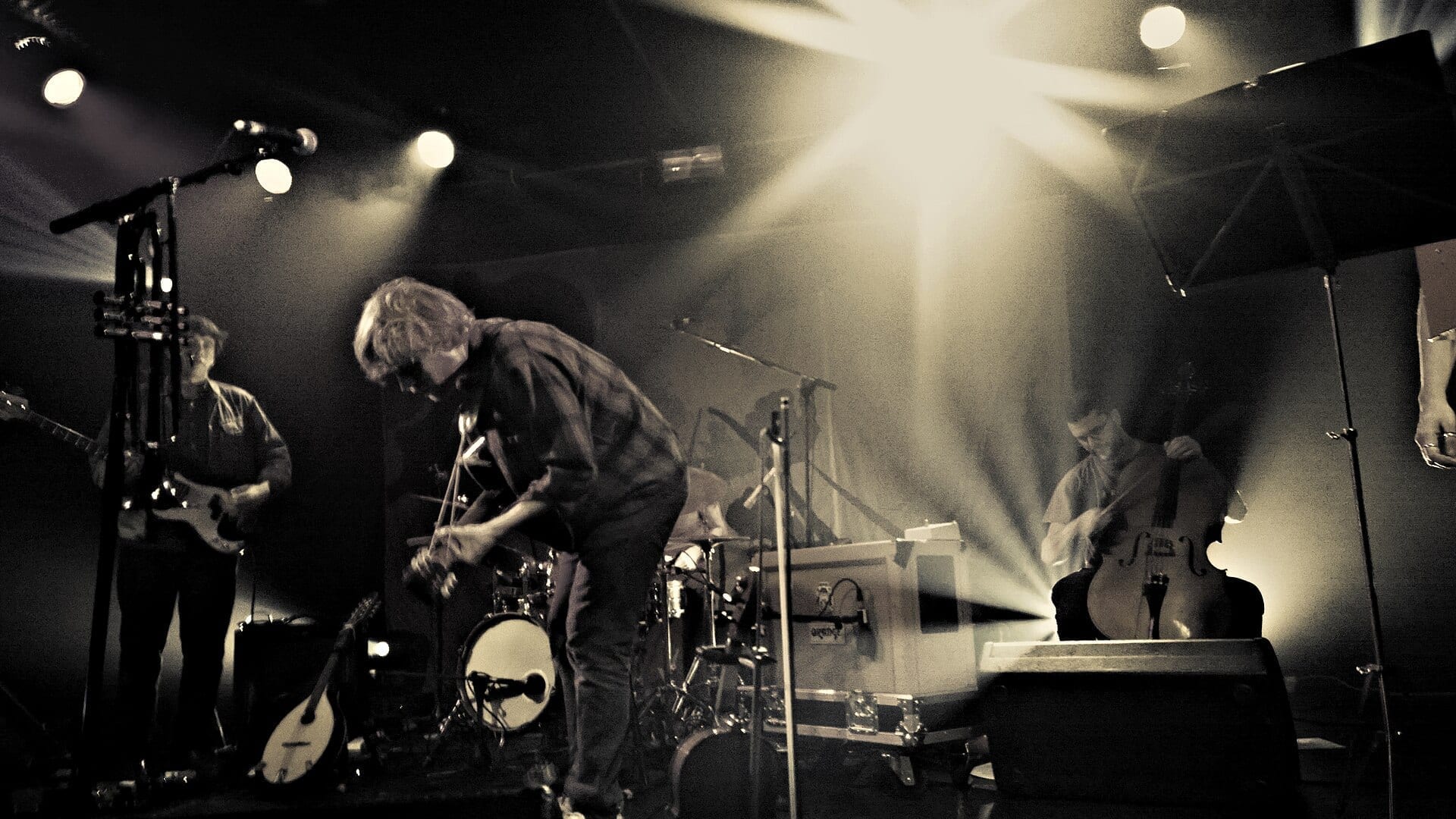 Johnny Flynn bends over his violin mid-song on a smoky, backlit stage, flanked by a guitarist and an upright bassist.