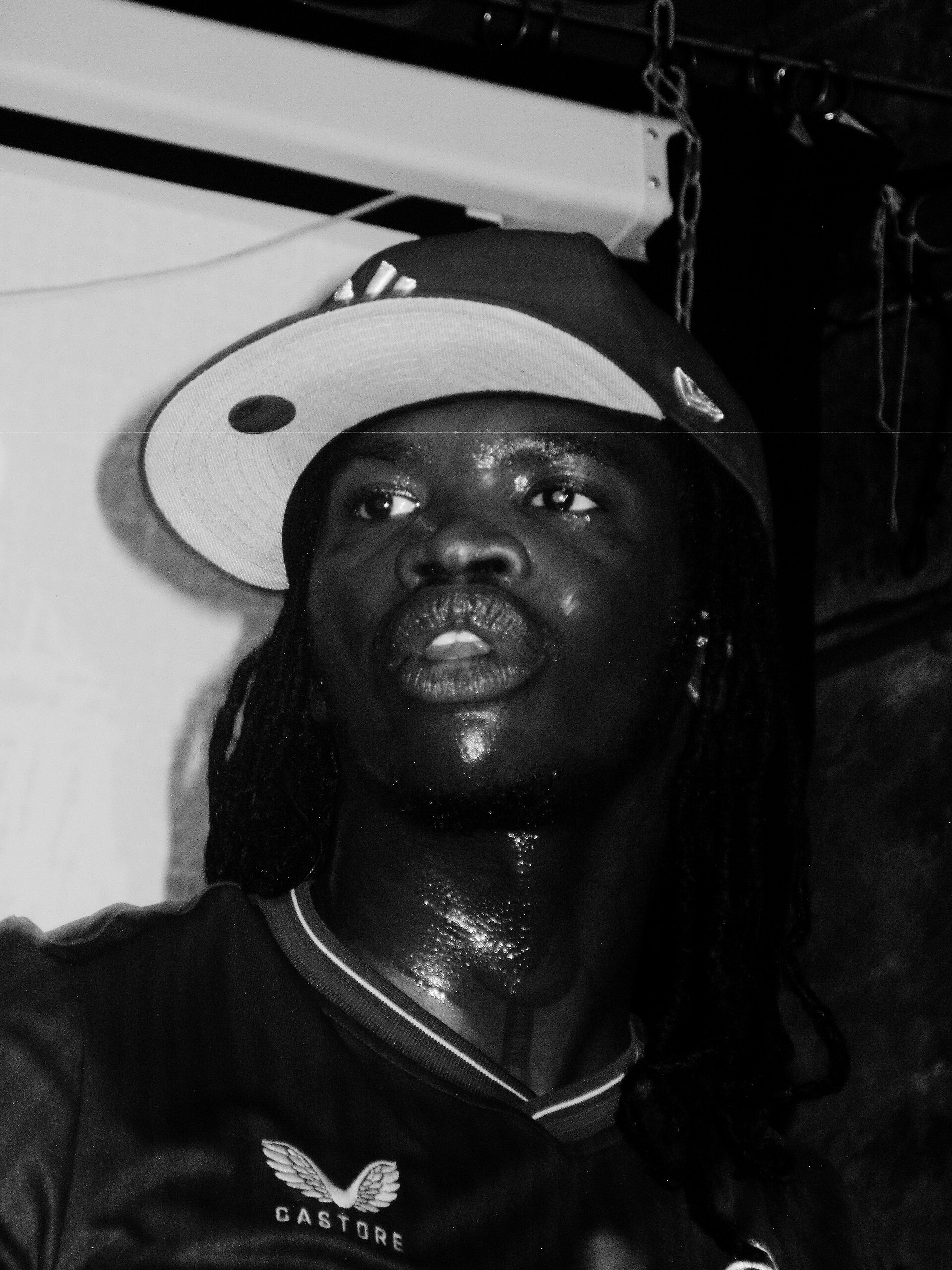 A black-and-white photograph of Lancey Foux looking up under stage lights in a white bucket hat and a dark top.