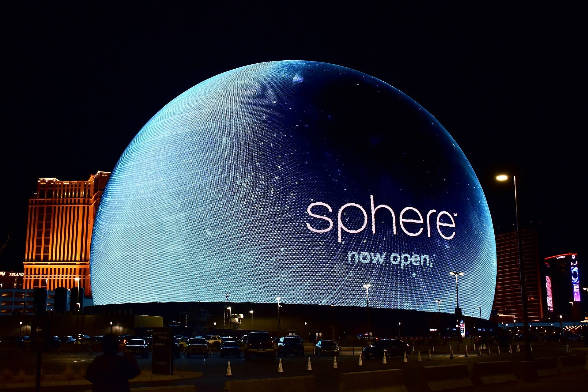 The Sphere in Las Vegas lit up at night, its curved exterior displaying a starfield and the word sphere, now open, beside the Las Vegas Strip skyline.