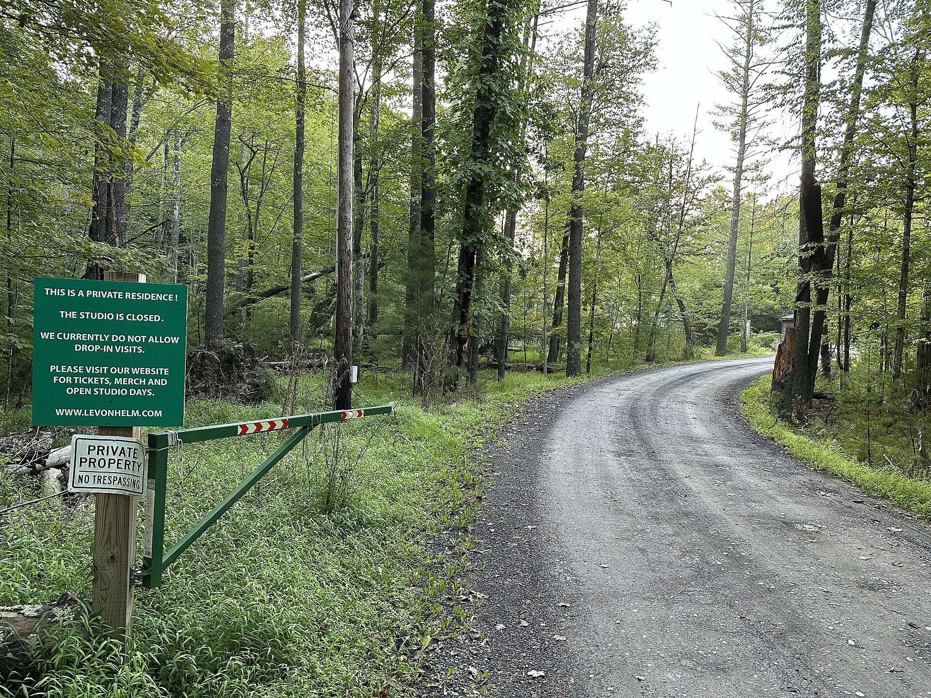 A gravel drive curving into woodland past a green gate and a sign reading that the studio is closed and drop-in visits are not allowed.