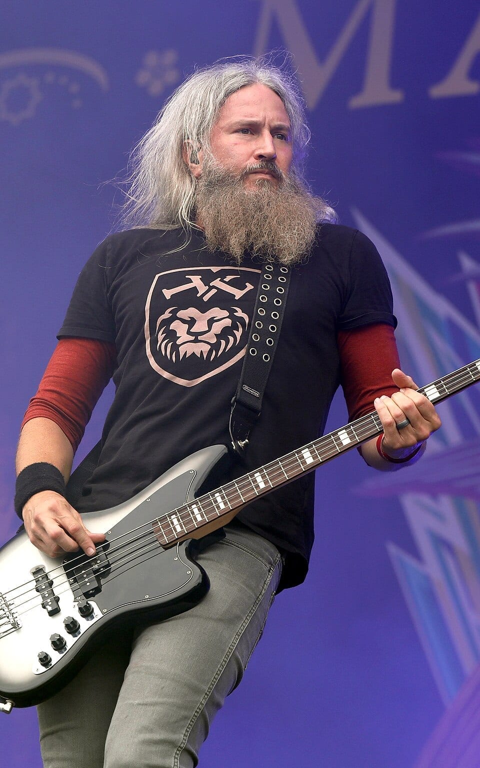 Troy Sanders of Mastodon plays a silver bass guitar on stage in front of a purple backdrop.