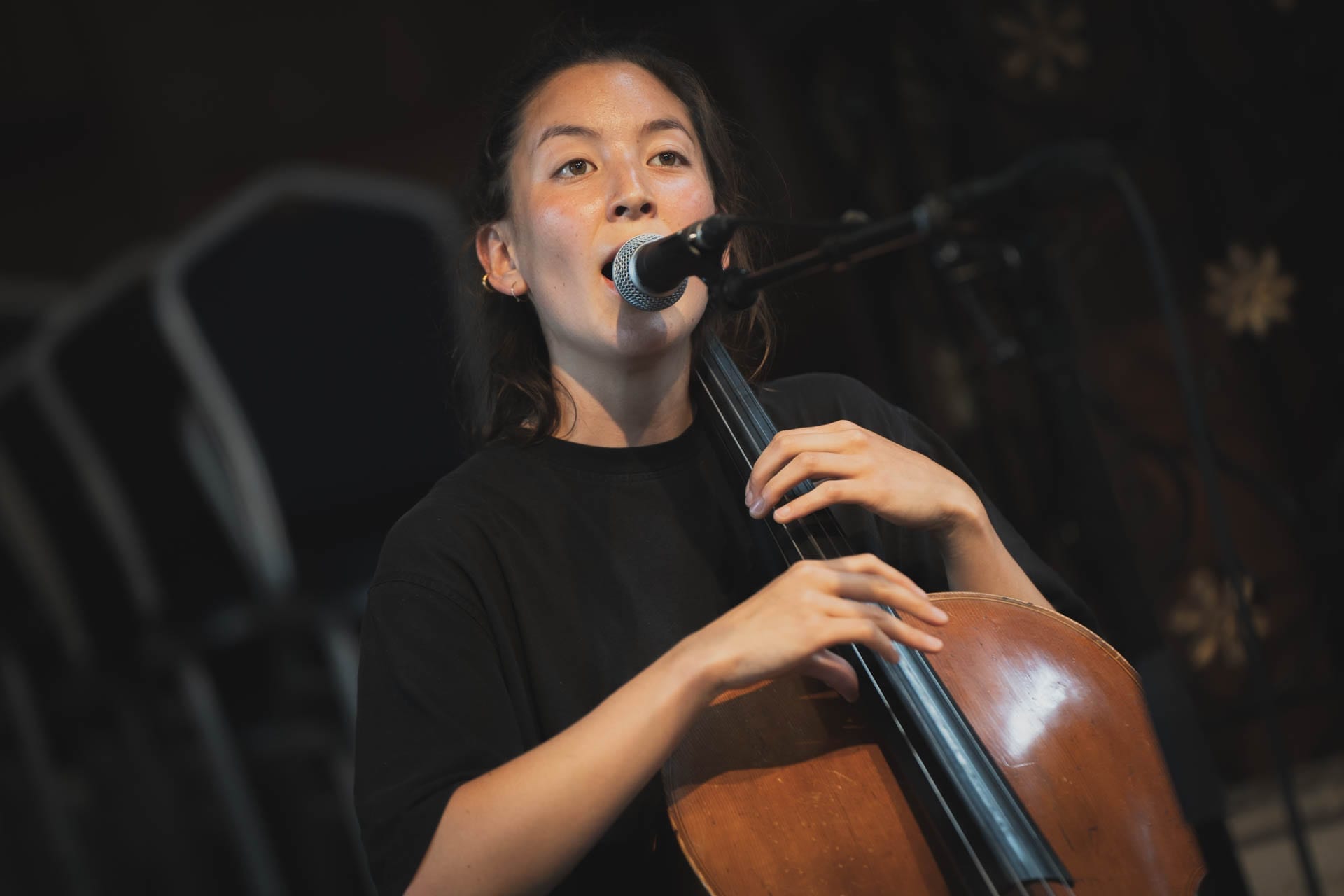 midori jaeger singing into a microphone while playing a cello on stage.