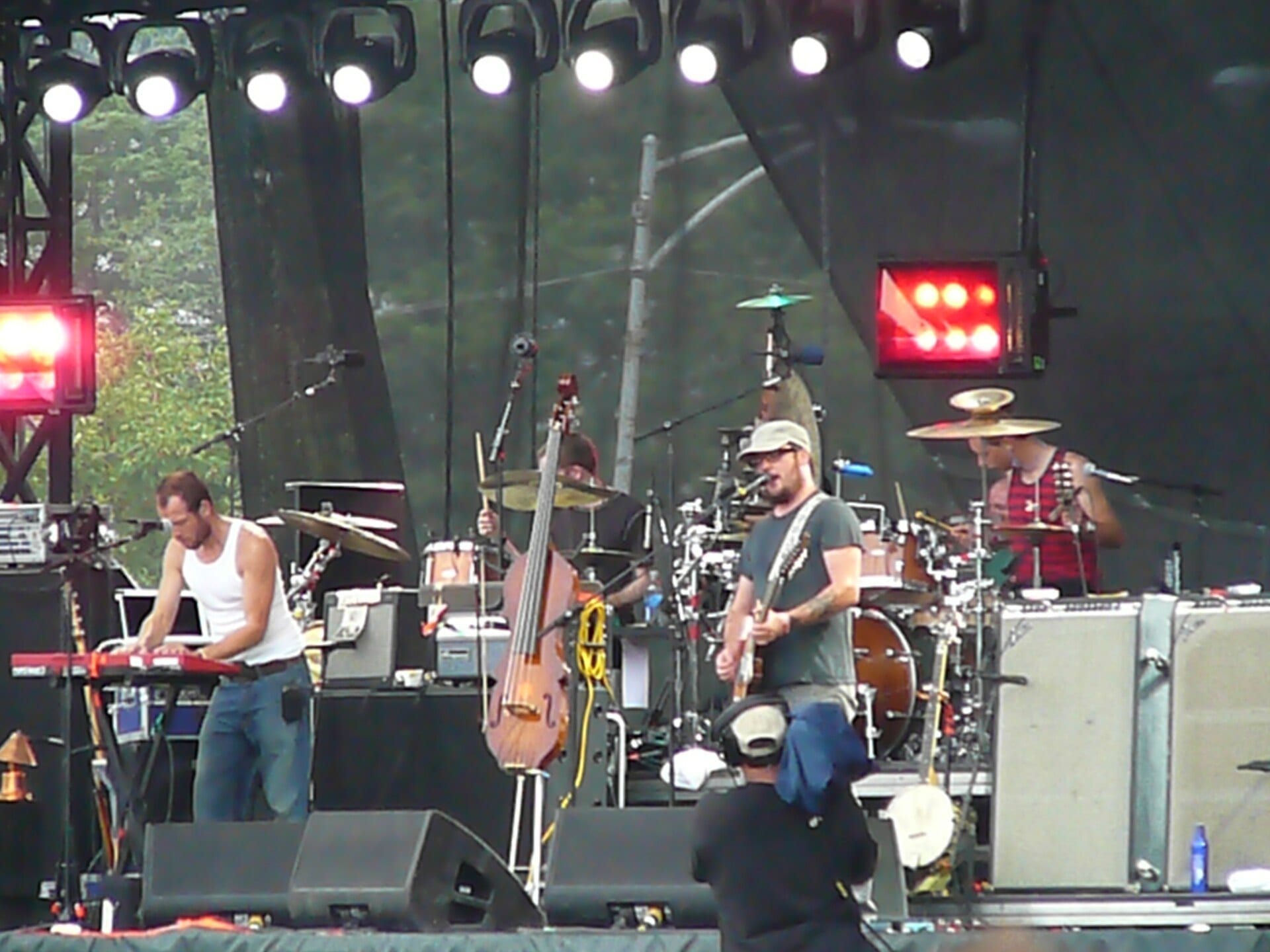 Modest Mouse performs on an outdoor festival stage, with a singer-guitarist at center, an upright bass and full drum kit visible behind him.