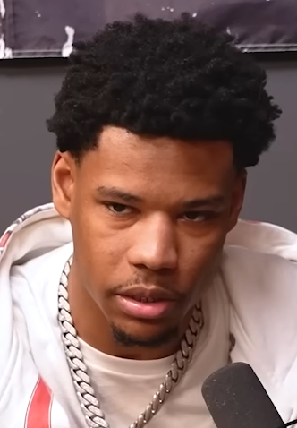 Nardo Wick speaks toward a podcast microphone in a white hoodie and a heavy silver chain.