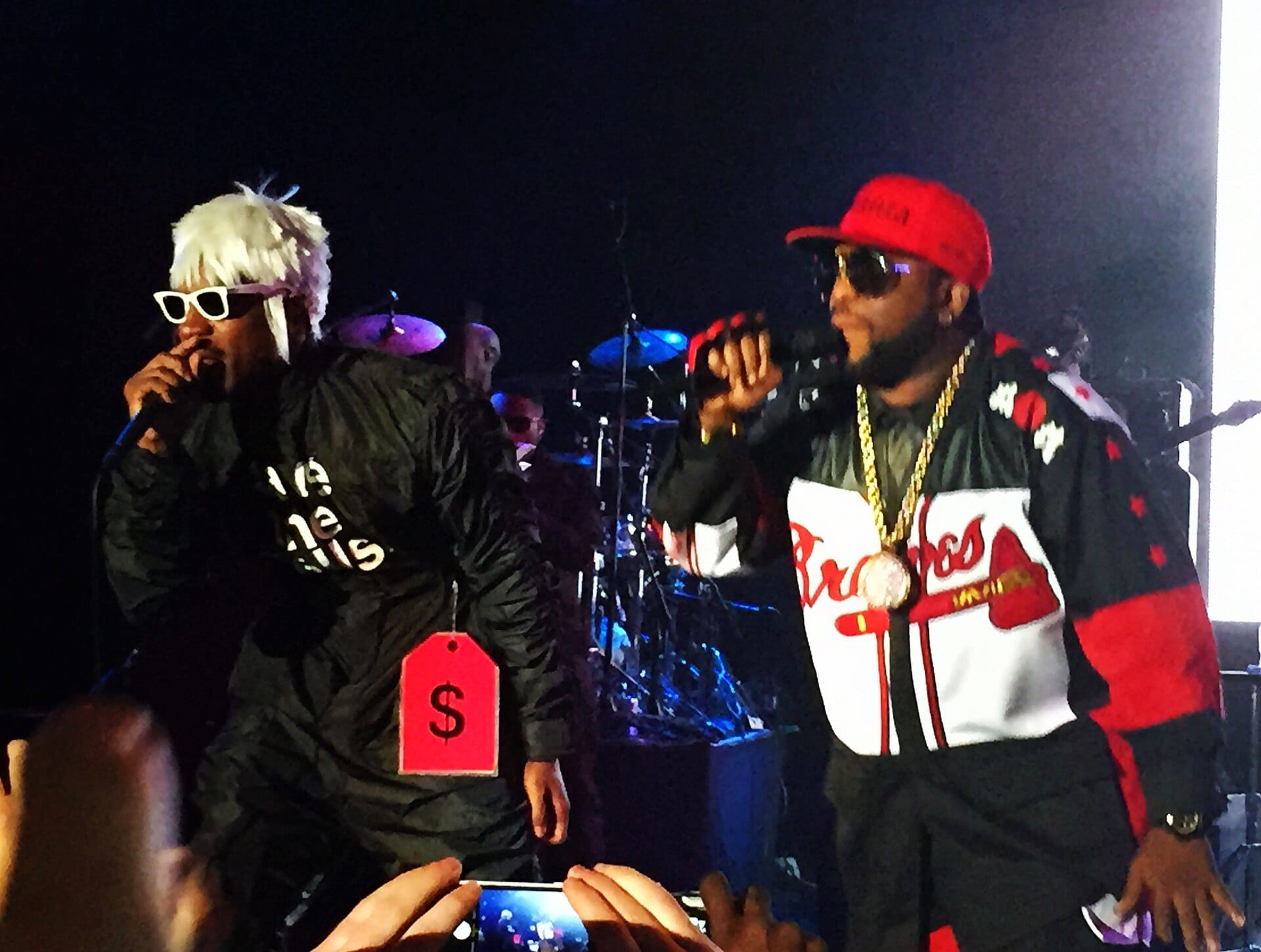 Andre 3000, in a platinum wig, white sunglasses and a jumpsuit hung with an oversized red price tag, raps beside Big Boi in a red cap and Atlanta Braves jacket with a gold chain.