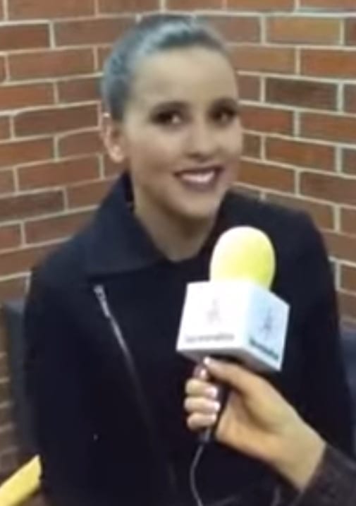 Paulina Goto smiles while being interviewed with a branded microphone in front of a brick wall.
