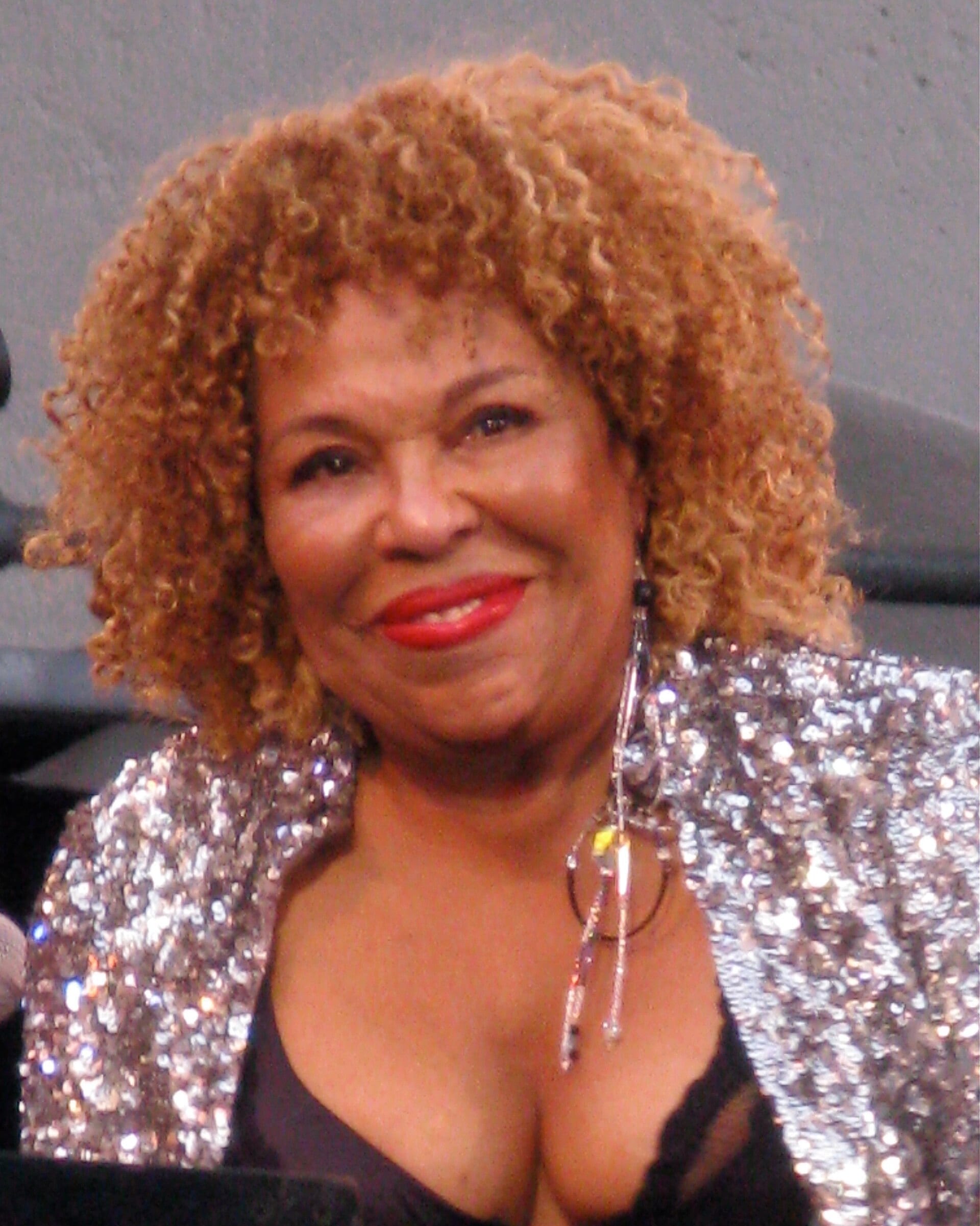 Roberta Flack smiles in a silver sequinned jacket and long crystal earrings, her blonde curls loose.