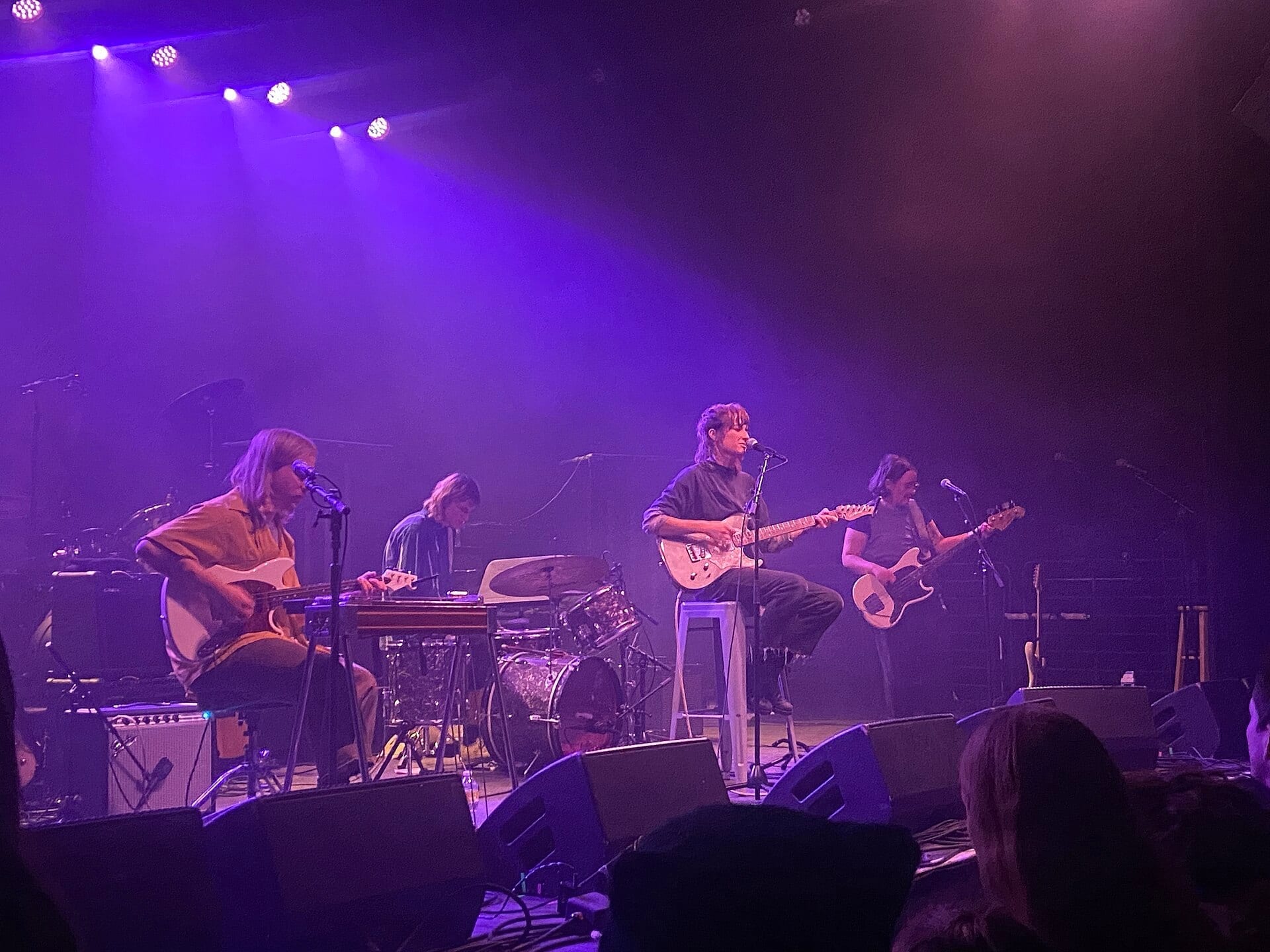 The four members of Sadurn perform on a small stage under purple lighting, with two guitarists seated on stools, a drummer, and a bassist standing at the right.
