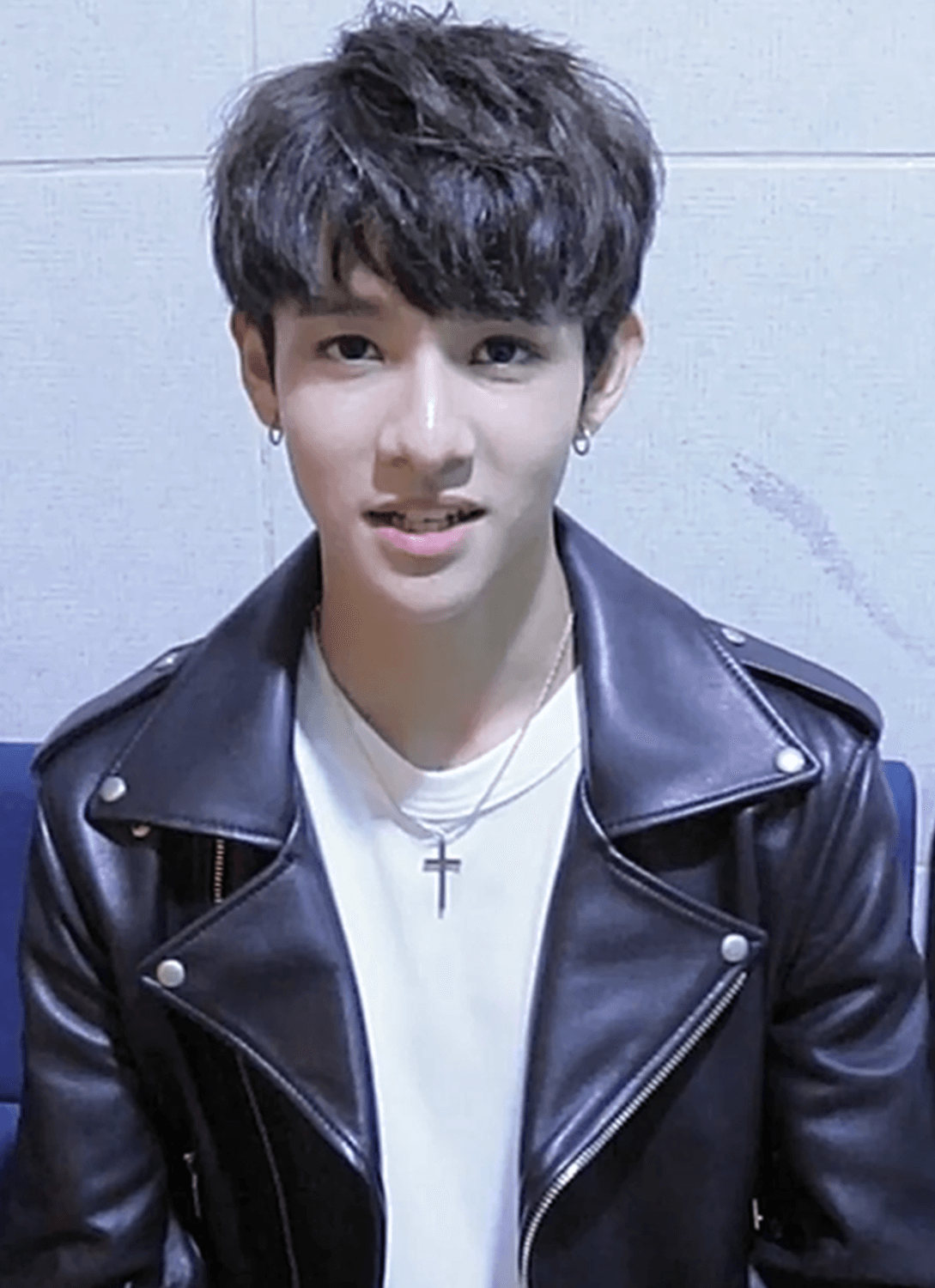 Samuel Kim, in a black leather jacket and a cross necklace, looks at the camera backstage.