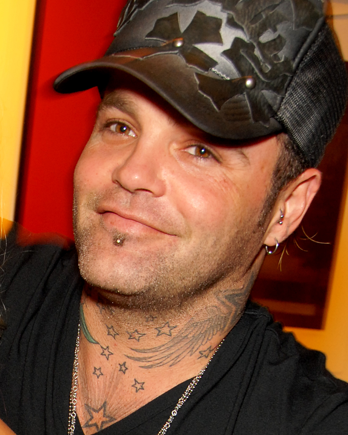 Shifty Shellshock looks at the camera in a flat cap and dark jacket, star tattoos visible on his neck.