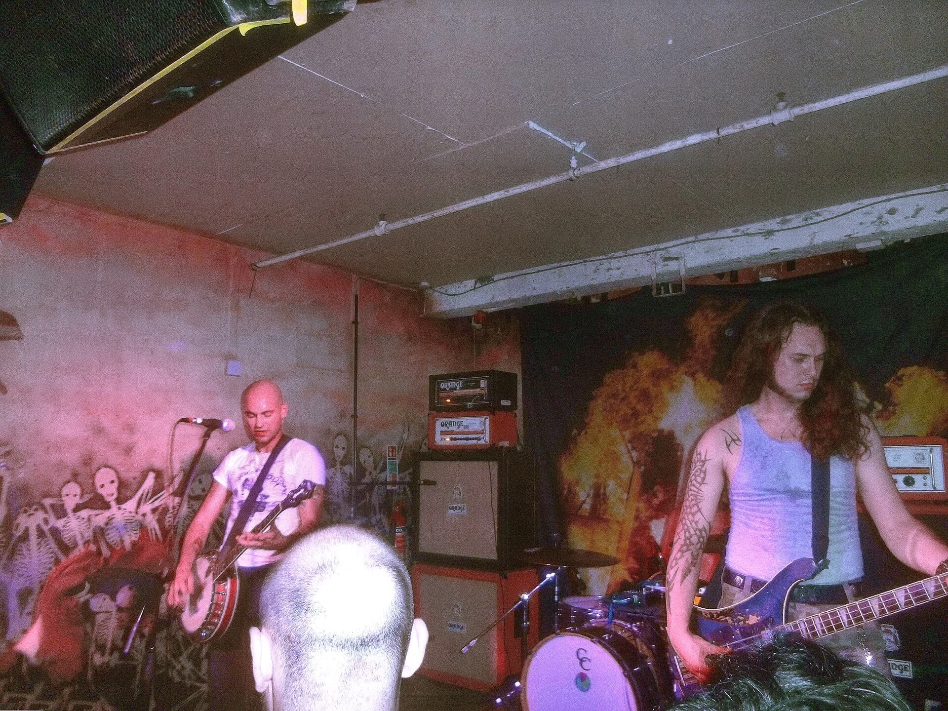 Show Me the Body performing in a small basement venue with skeleton mural artwork, a bassist and guitarist playing on either side of the drummer.