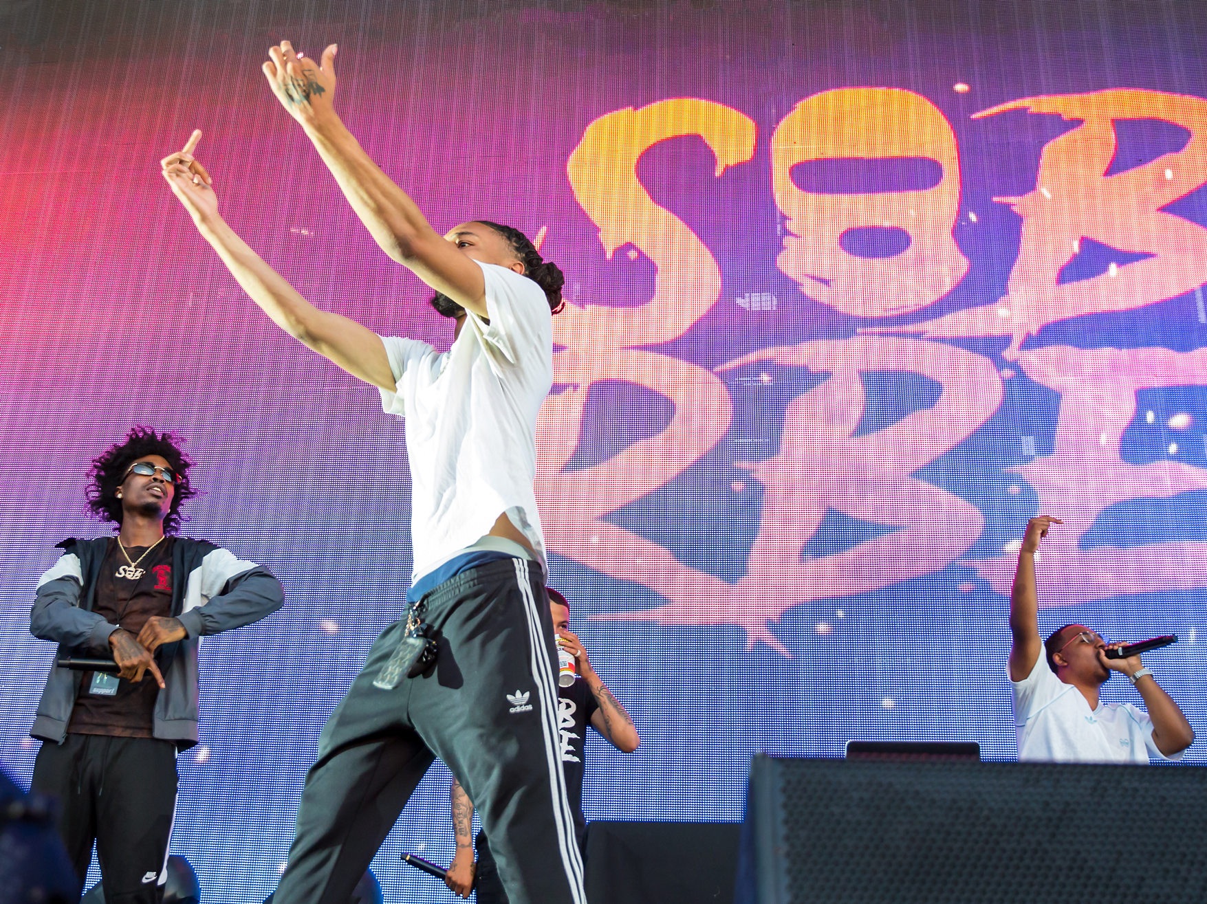 Members of SOB x RBE rap across the front of an amphitheatre stage, the group's name lit on the screen behind them.