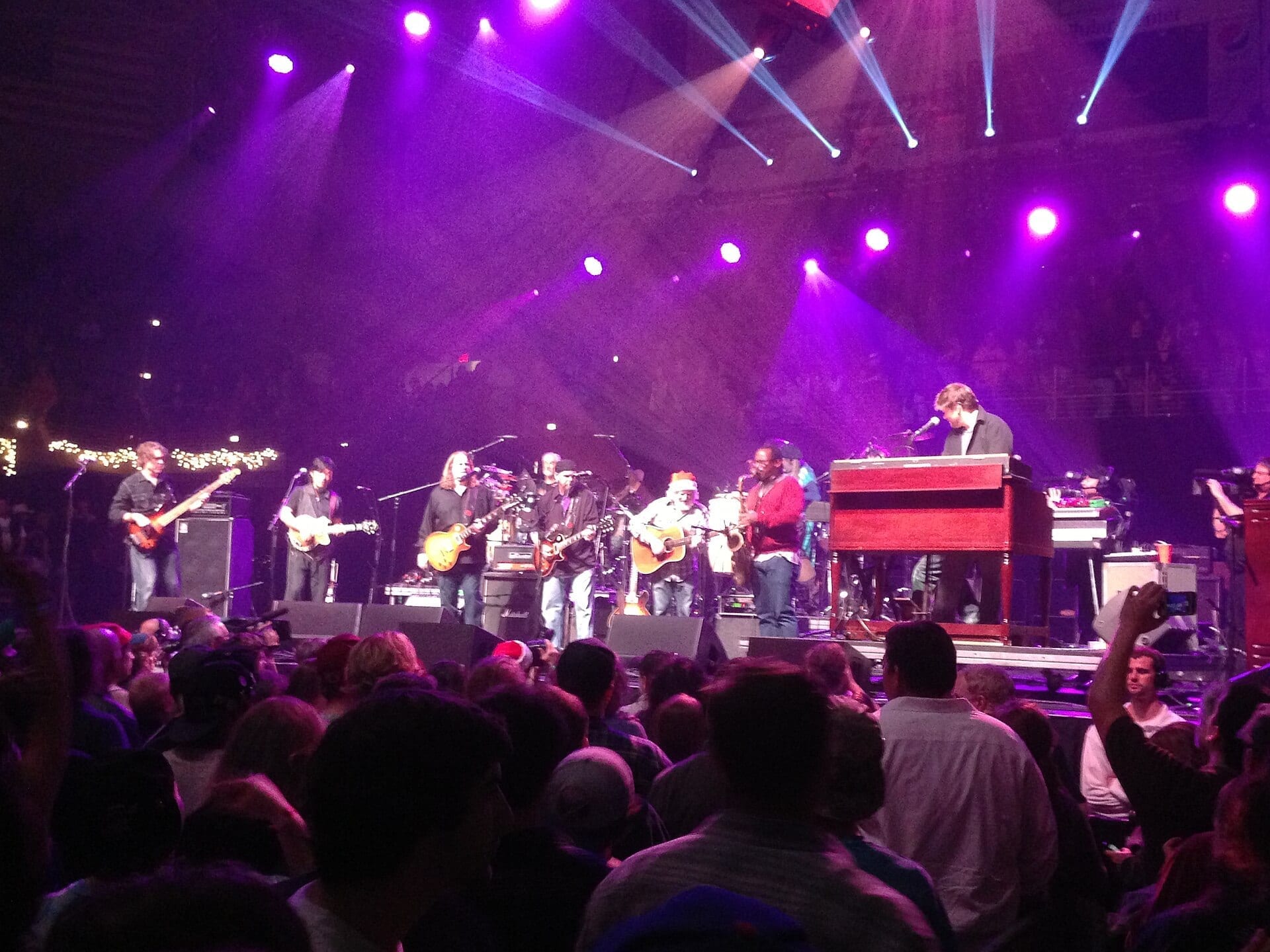 The String Cheese Incident joins a large ensemble of guitarists, a saxophonist and an organist on a purple-lit stage above a packed crowd.