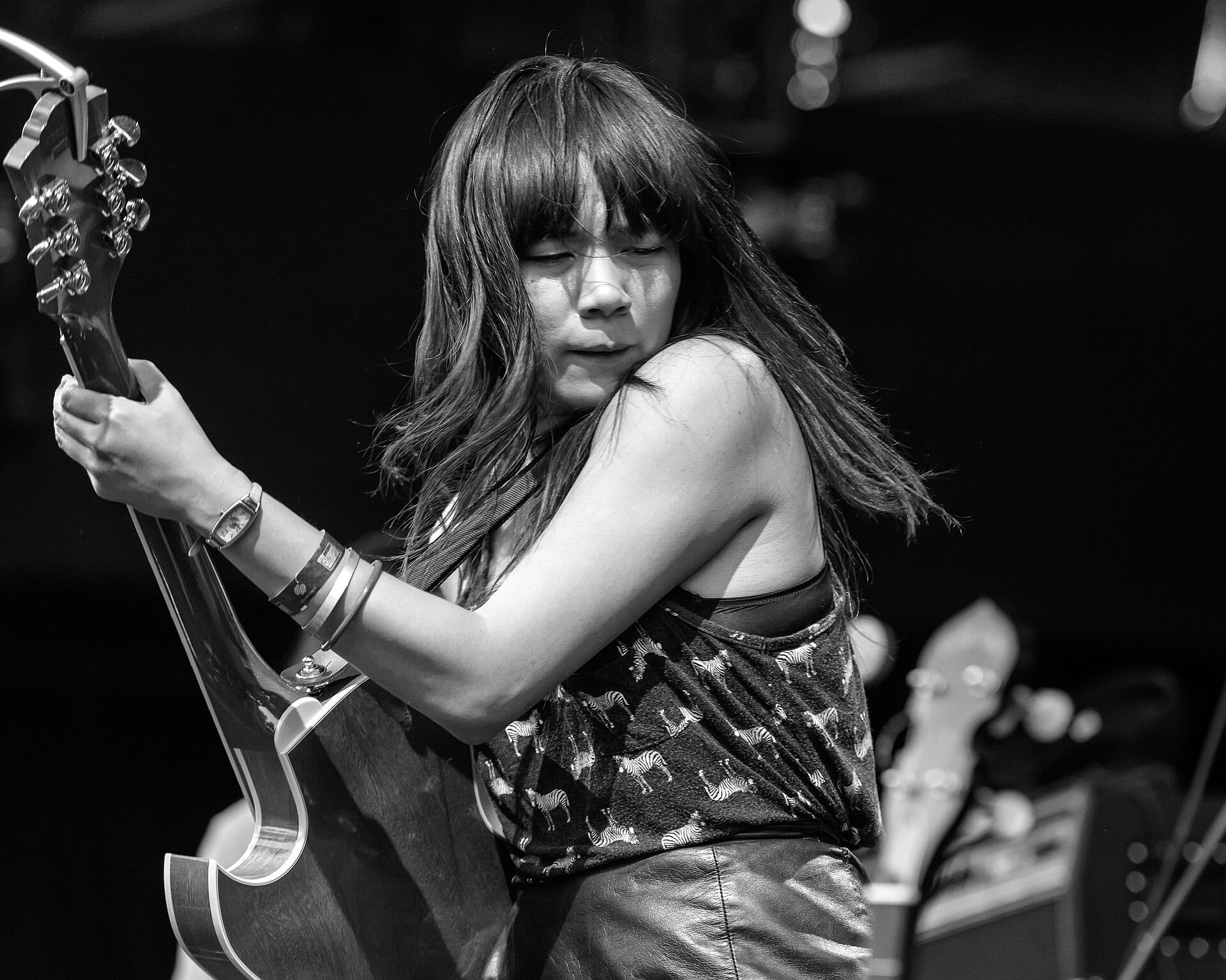 A black-and-white shot of Thao Nguyen leaning into her guitar with eyes shut, long dark hair swinging, wearing a zebra-print top and leather trousers.
