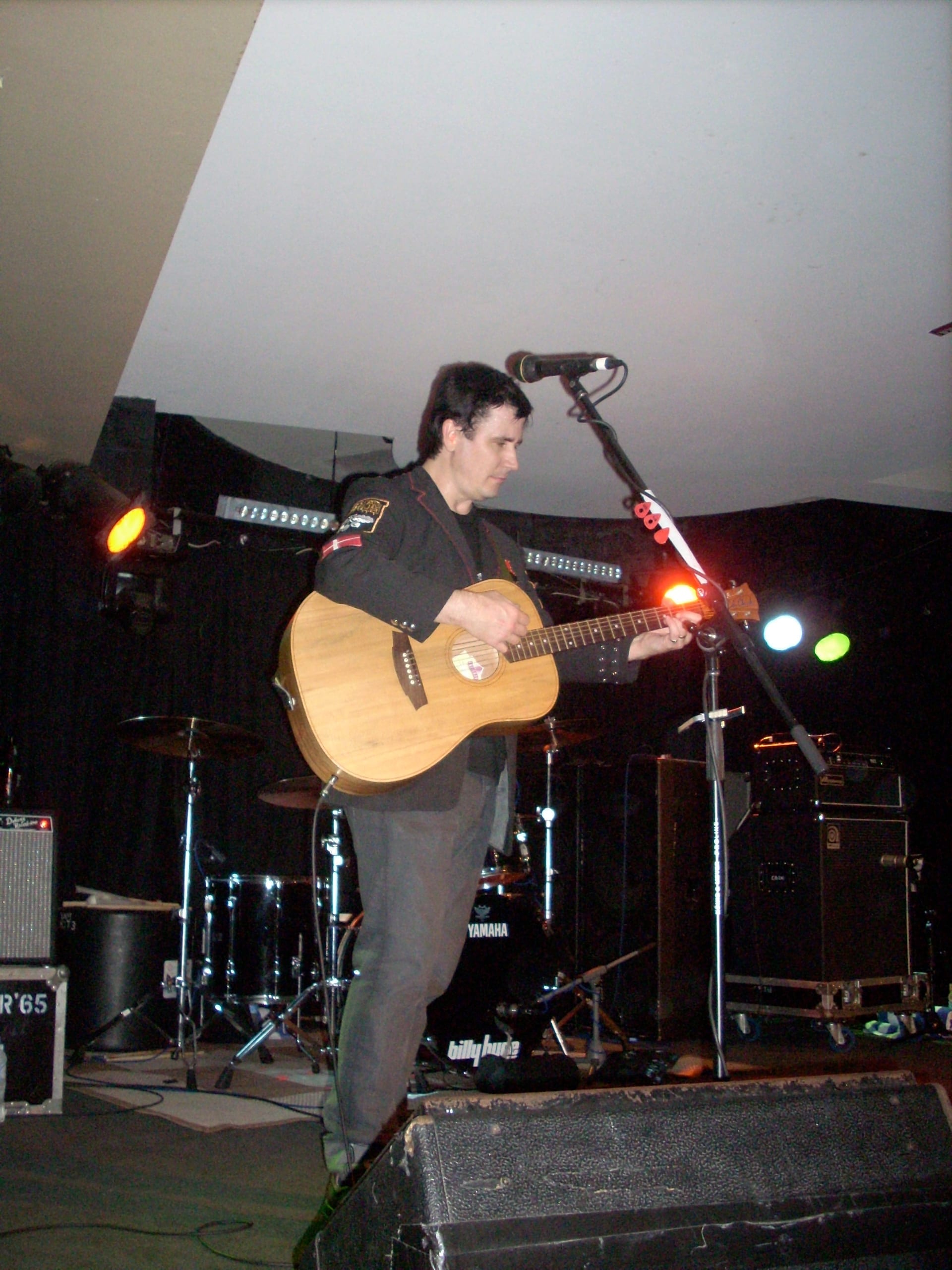 John Darnielle of the Mountain Goats plays an acoustic guitar in front of a microphone on a small stage.