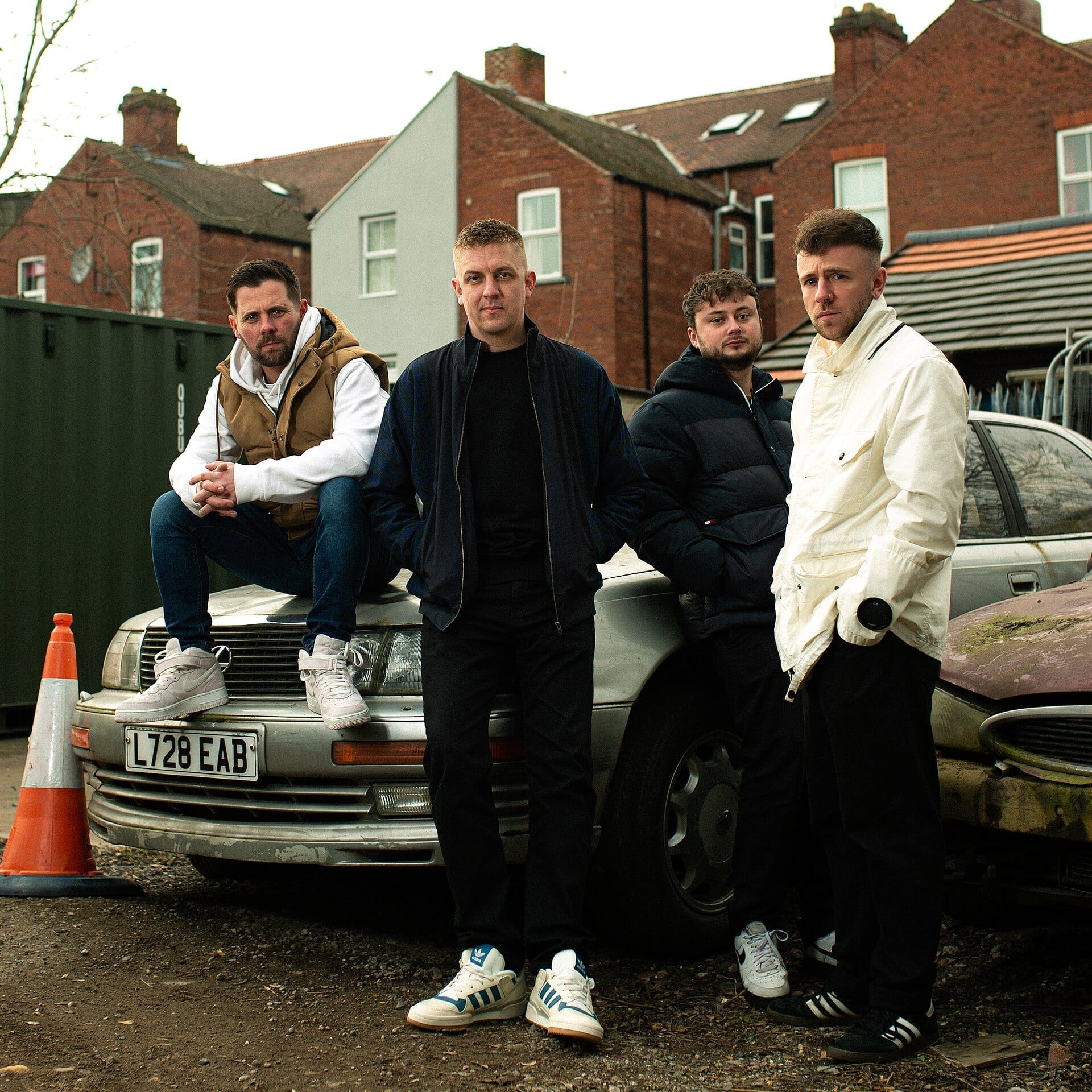 The four members of indie rock band The Reytons pose around an old car parked in a UK residential street, one sitting on the bonnet.