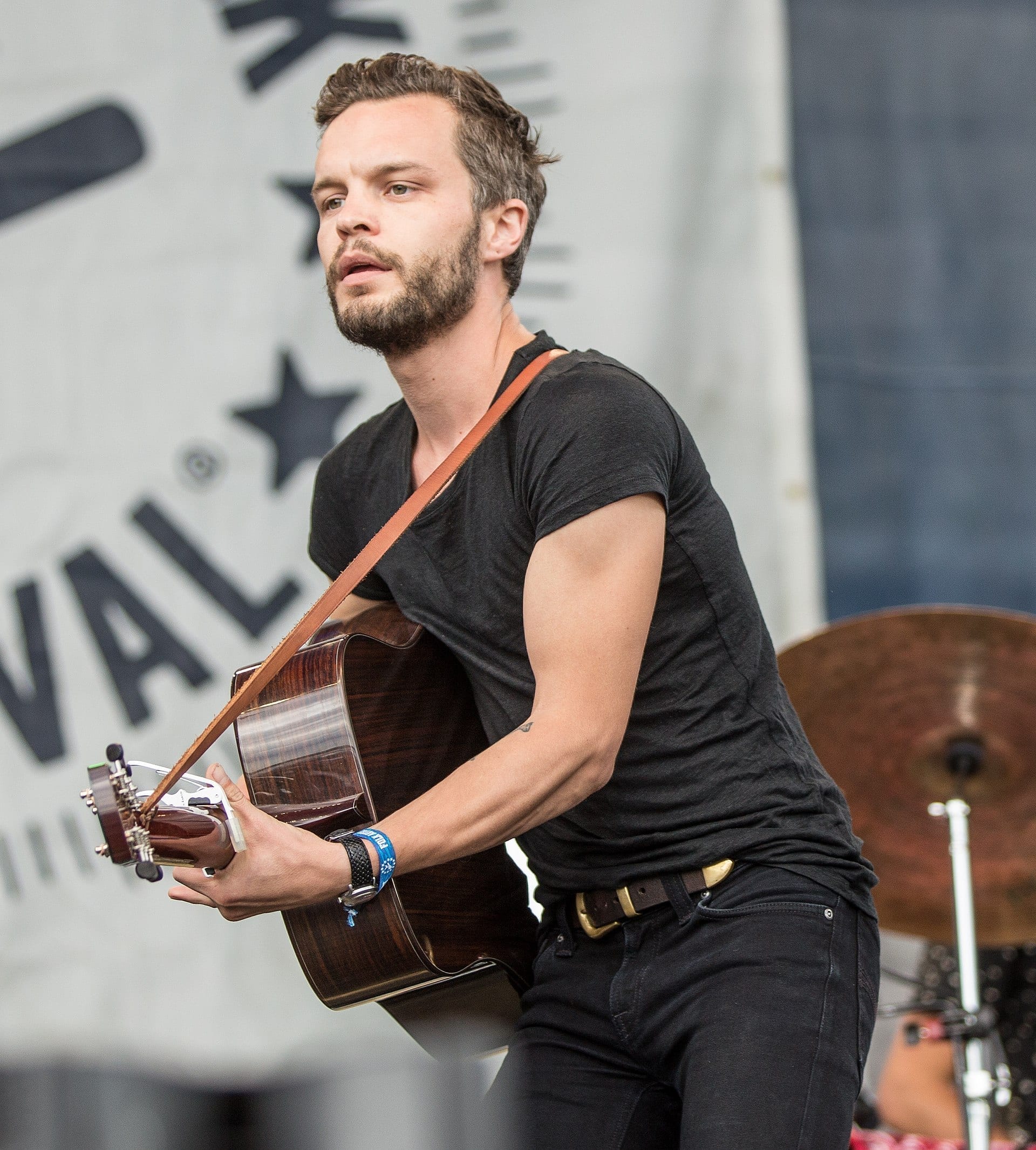 Kristian Matsson, The Tallest Man on Earth, plays an acoustic guitar on an outdoor festival stage, wearing a black t-shirt.