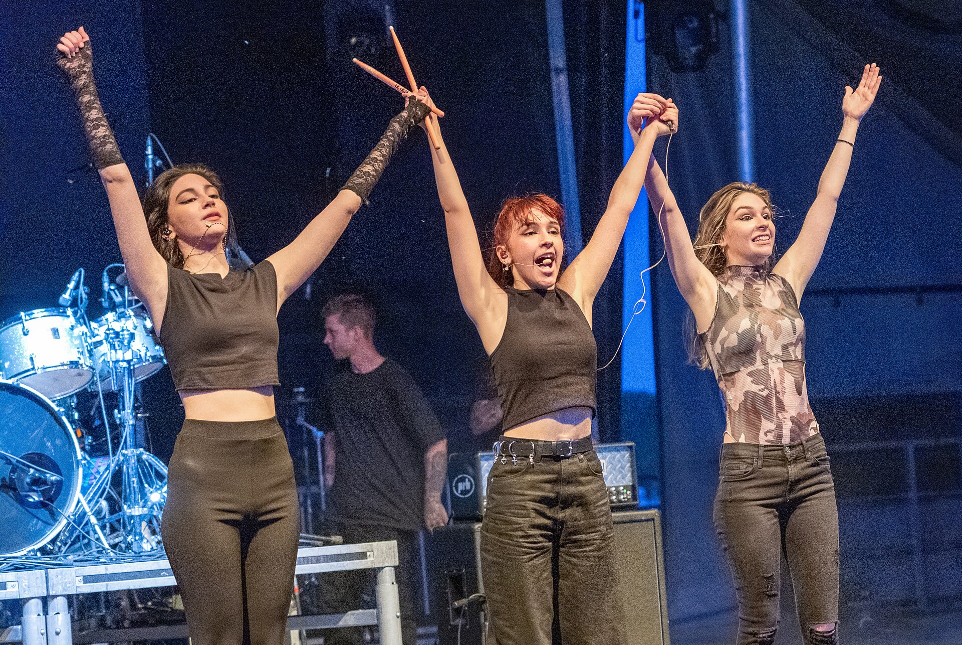 The three sisters of The Warning stand together with arms raised after a show, one holding drumsticks.