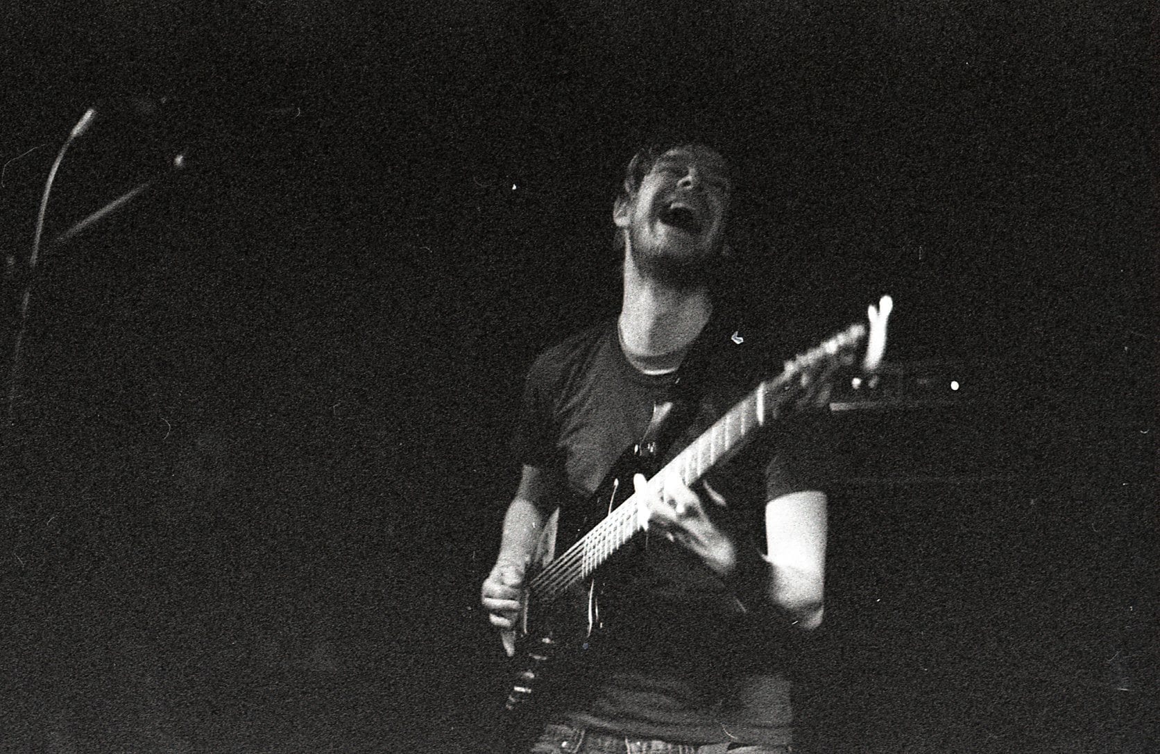 A guitarist from TTNG plays with head tilted back mid-shout, in a grainy black and white live photo.