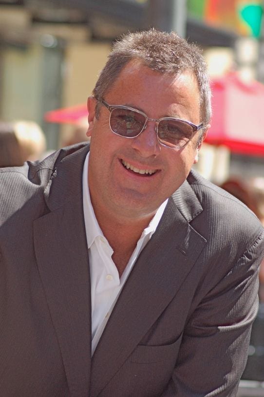 Vince Gill smiling in sunglasses and a dark suit at an outdoor ceremony.