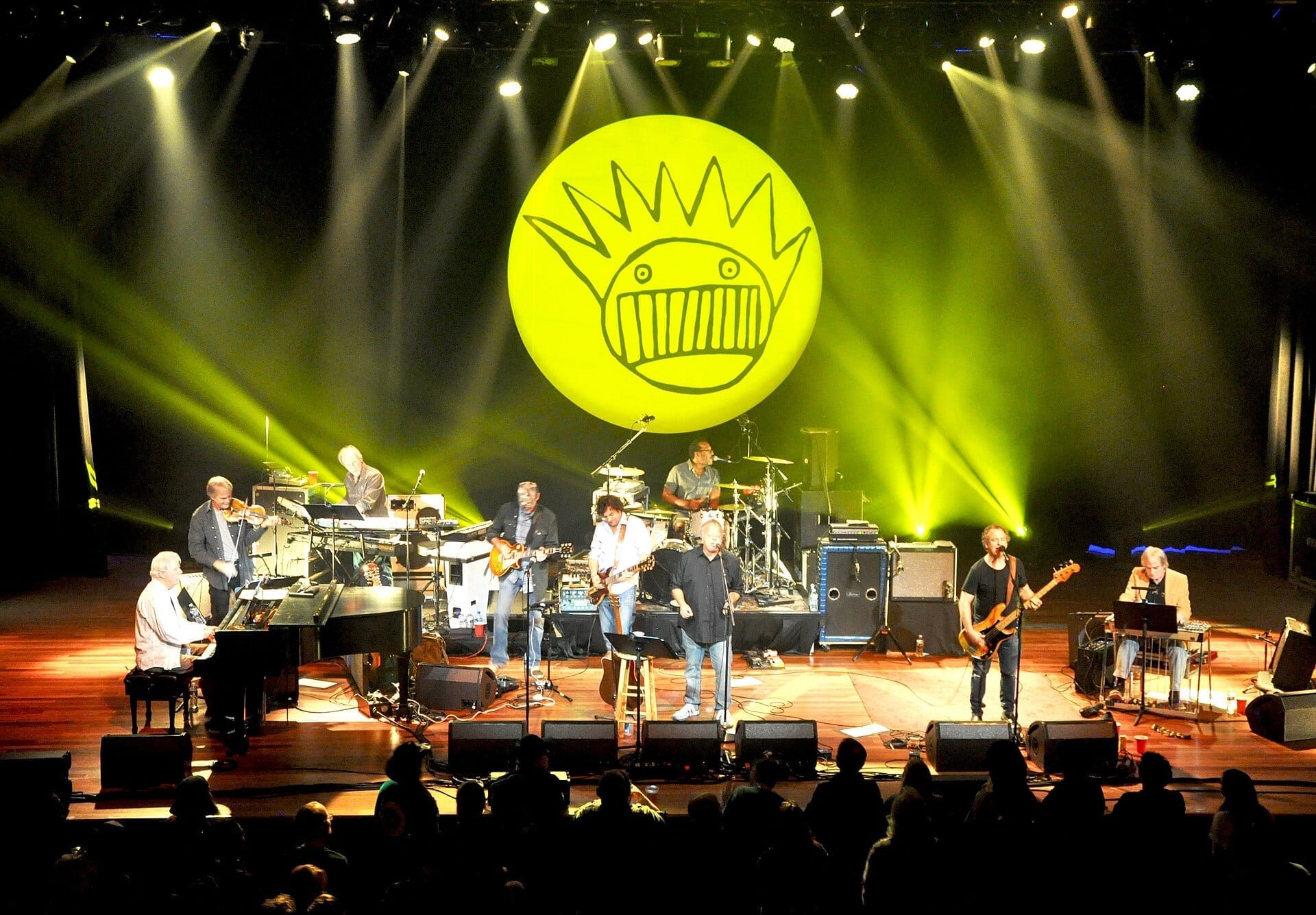 Ween performs on stage with an expanded backing band beneath a large illuminated Boognish logo at the Ryman Auditorium.