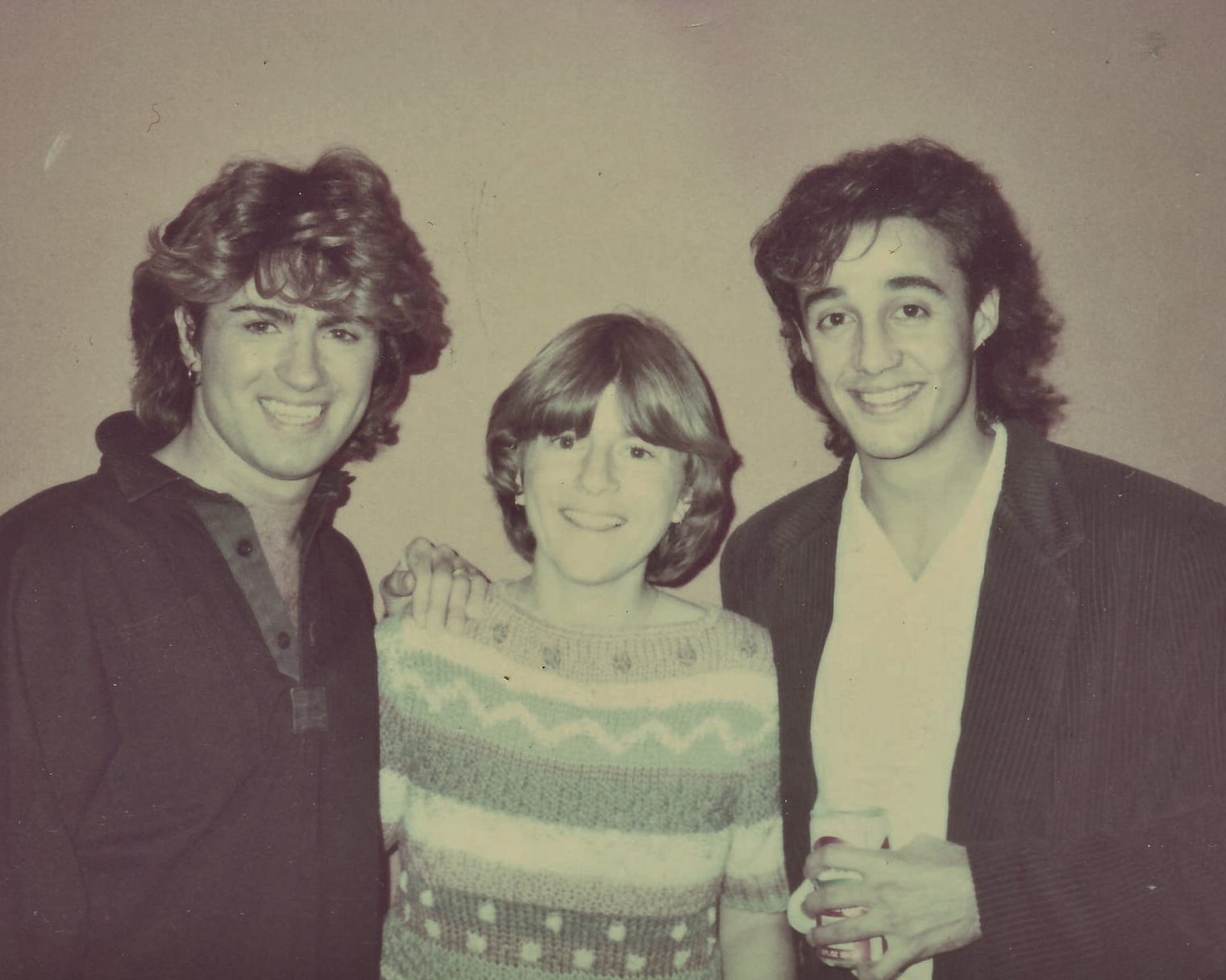A faded color snapshot of two young men with feathered hair standing on either side of a smiling woman.